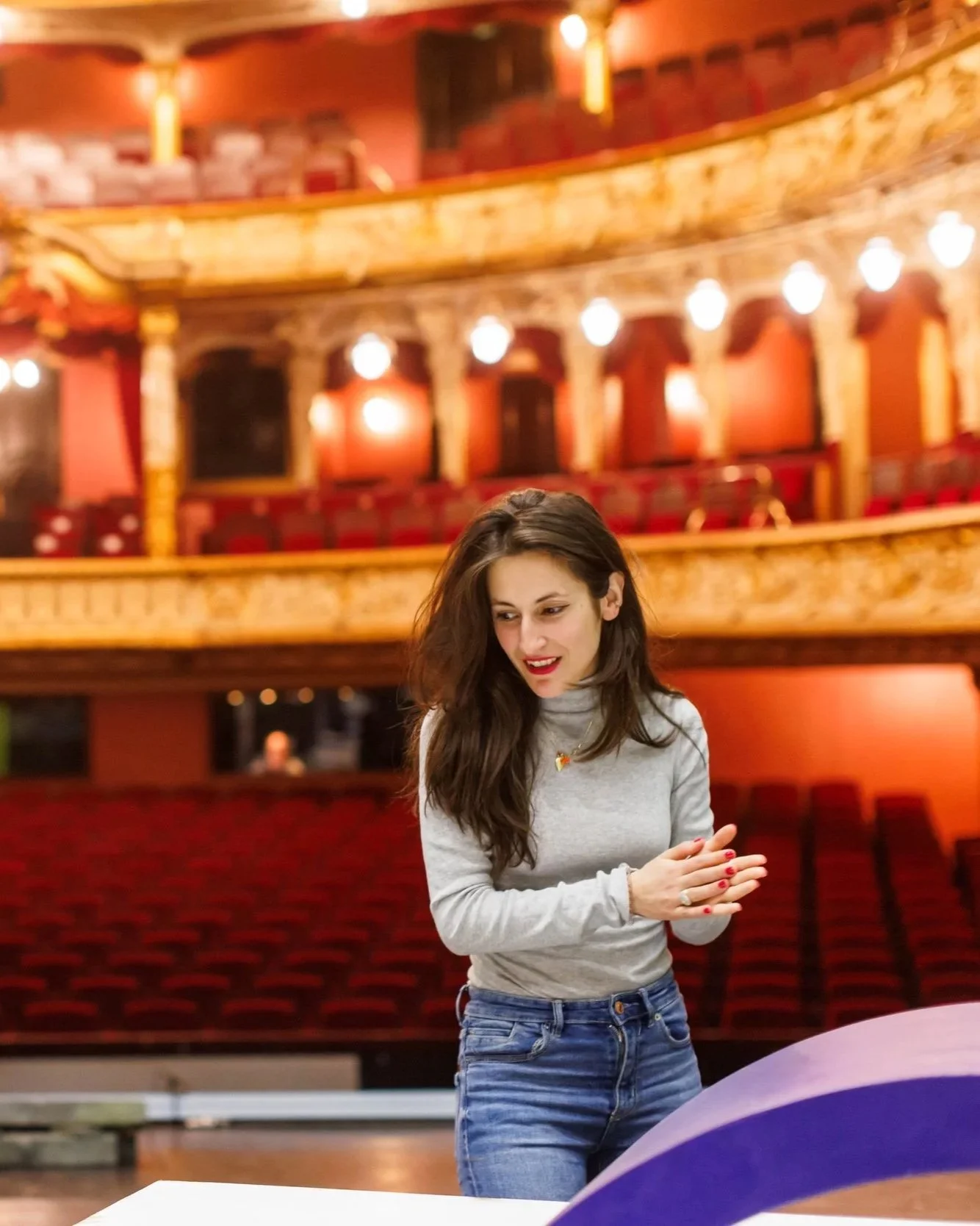 Junge Frau probiert in einem Theaterprobe einer großen, roten Theaterbühne und Sitzgelegenheiten im Hintergrund.