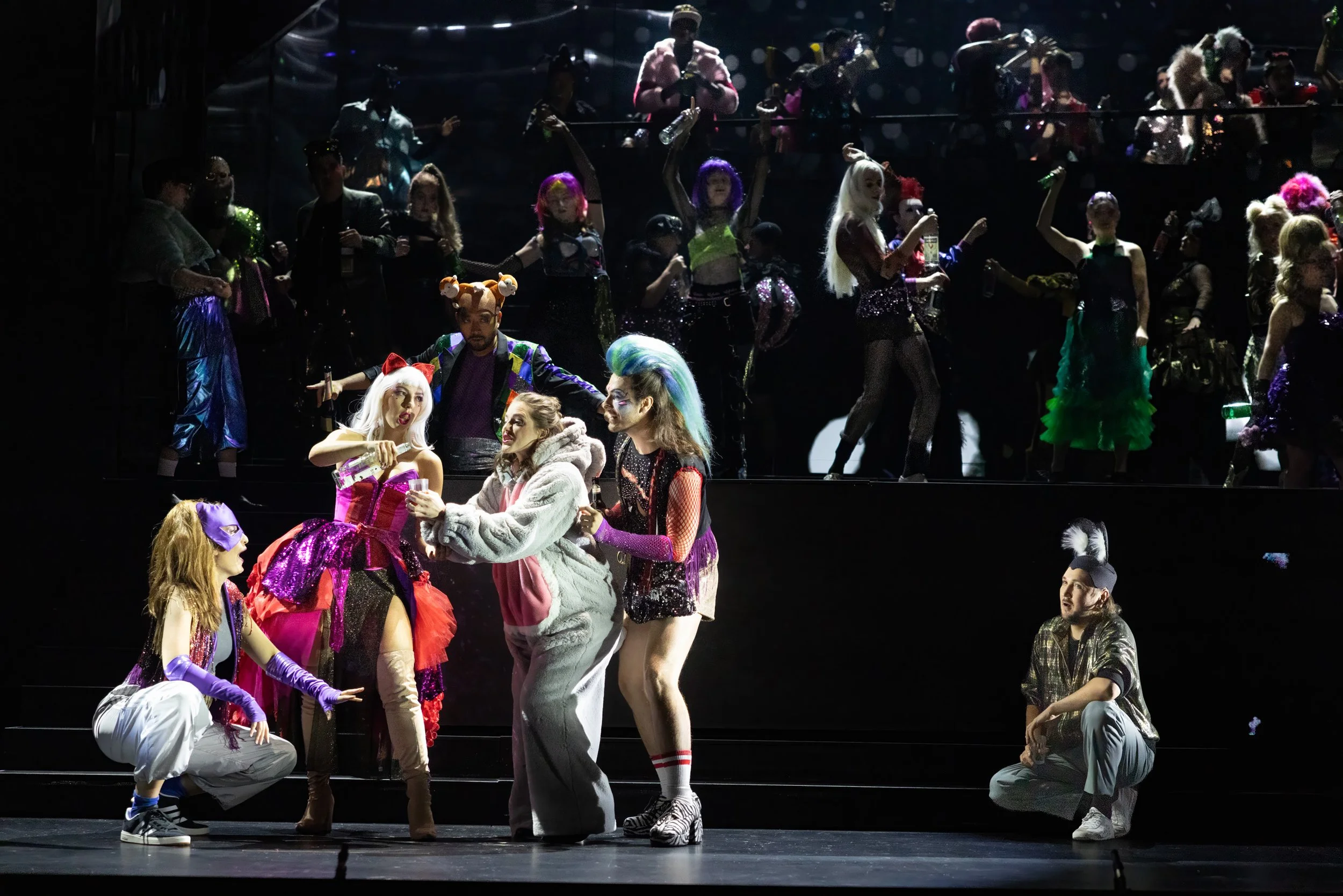 Bunte Darsteller in auffälligen Kostümen auf einer Theaterbühne, vermutlich bei einer Musical- oder Theateraufführung.