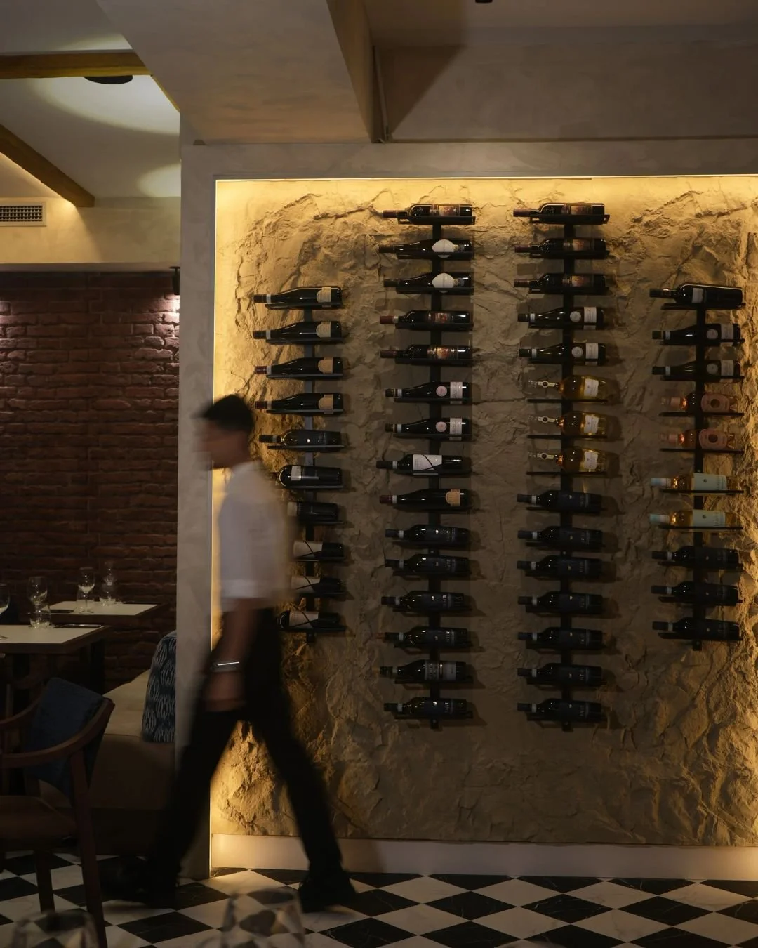 Estante de vinos en una bodega de un restaurante, con iluminación cálida en una pared de piedra.