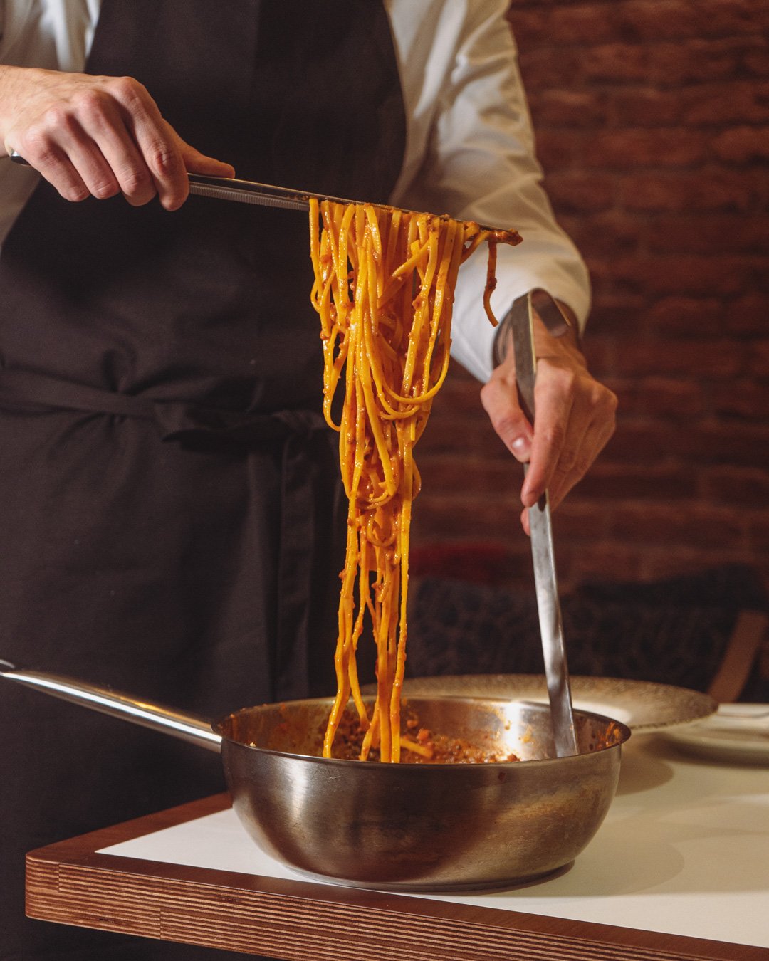 Chef sirviendo espaguetis en un bol de acero.