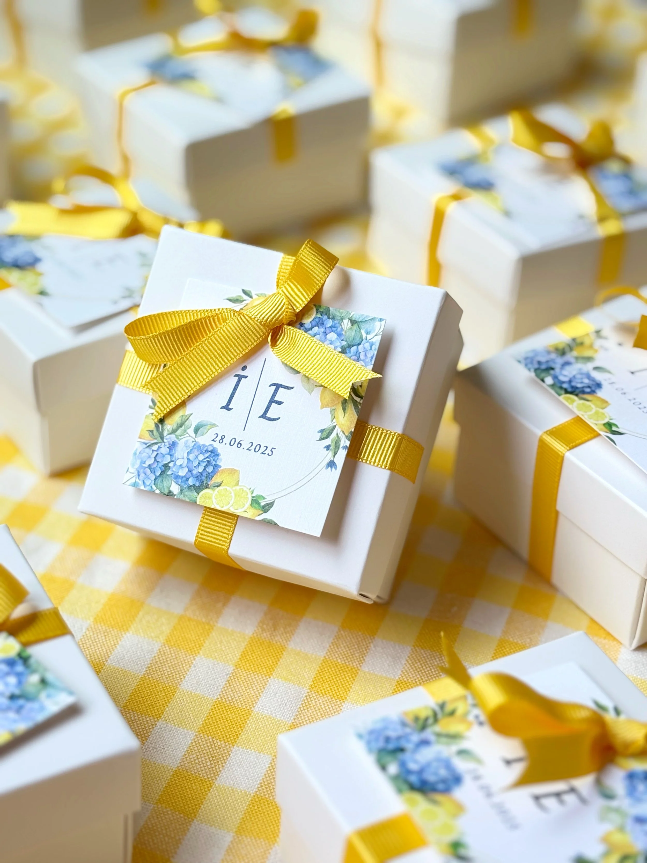 White gift boxes with yellow ribbons and floral labels, arranged on a yellow and white checkered tablecloth.