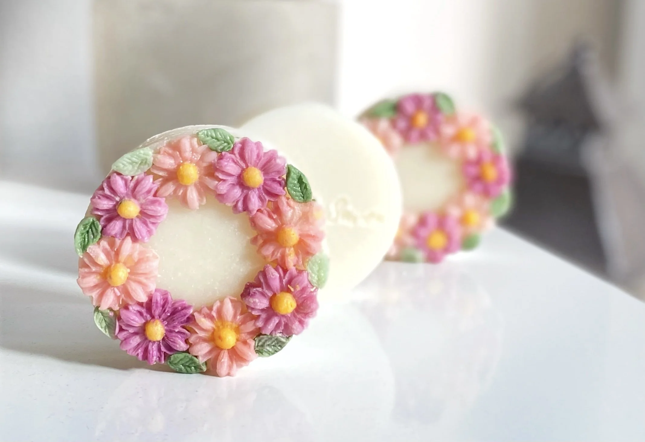 Three white round cookies decorated with pink and purple flowers and green leaves arranged in a heart shape.