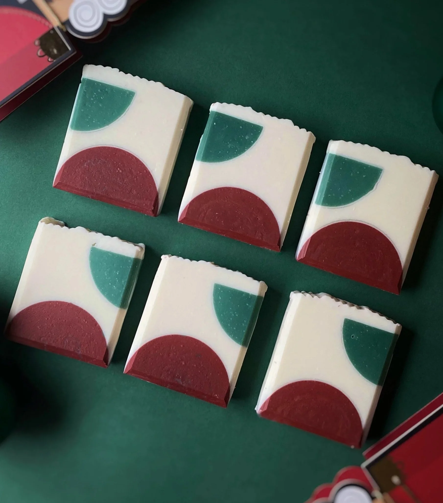 Six small decorative soap bars with a geometric design in red, green, and white, placed on a green surface.