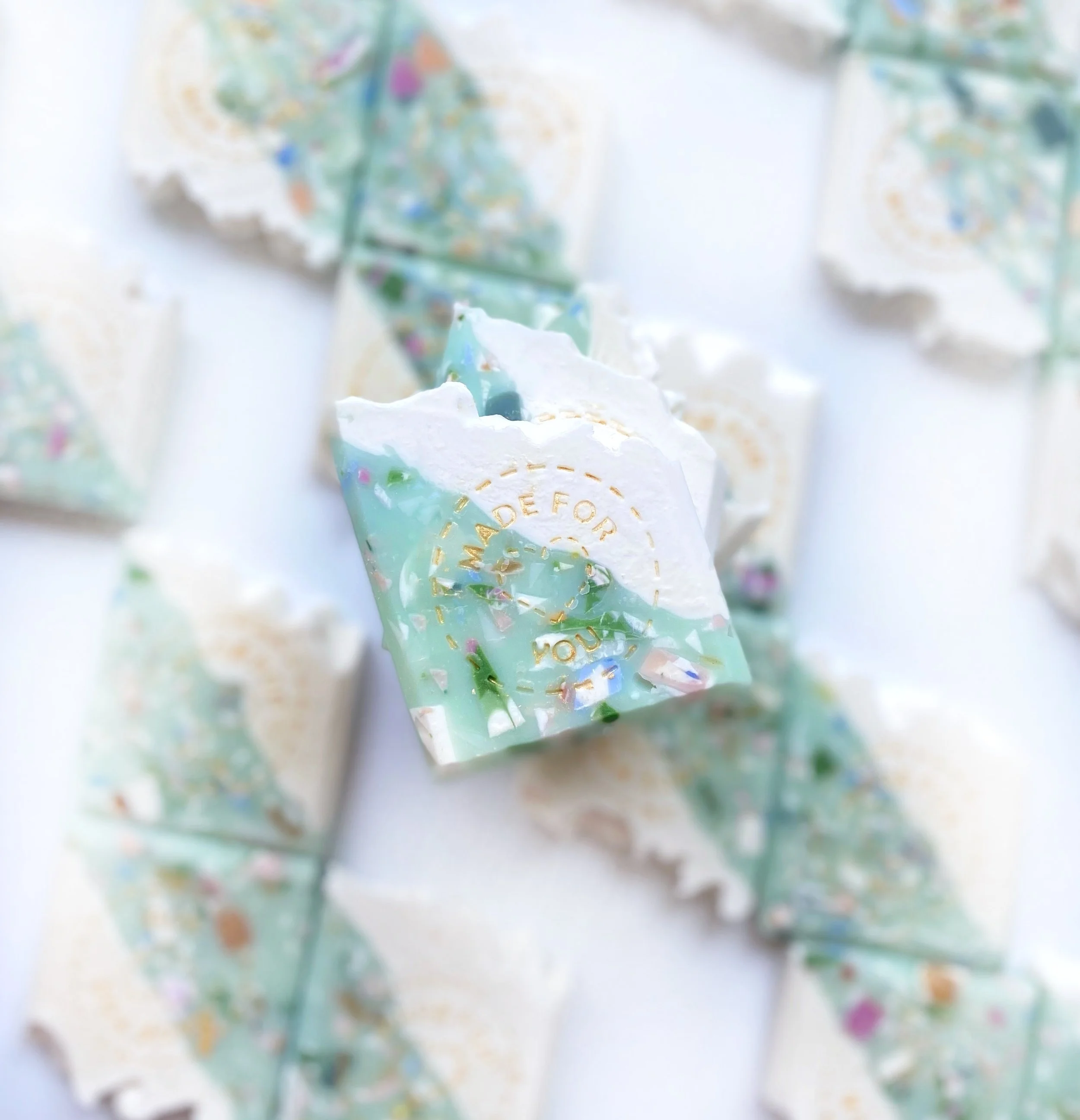 Colorful seashell-shaped soap with white, green, and multicolor swirls, and gold lettering that reads "Made for you".