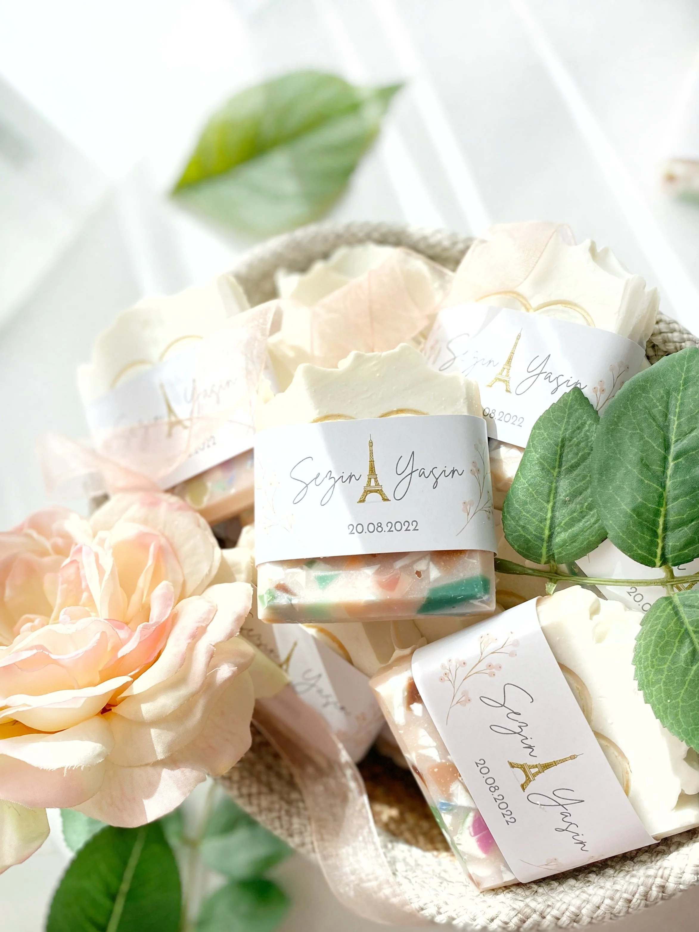 Soap bars with personalized labels featuring the Eiffel Tower and the date 20.08.2022, decorated with pink and cream flowers and green leaves.