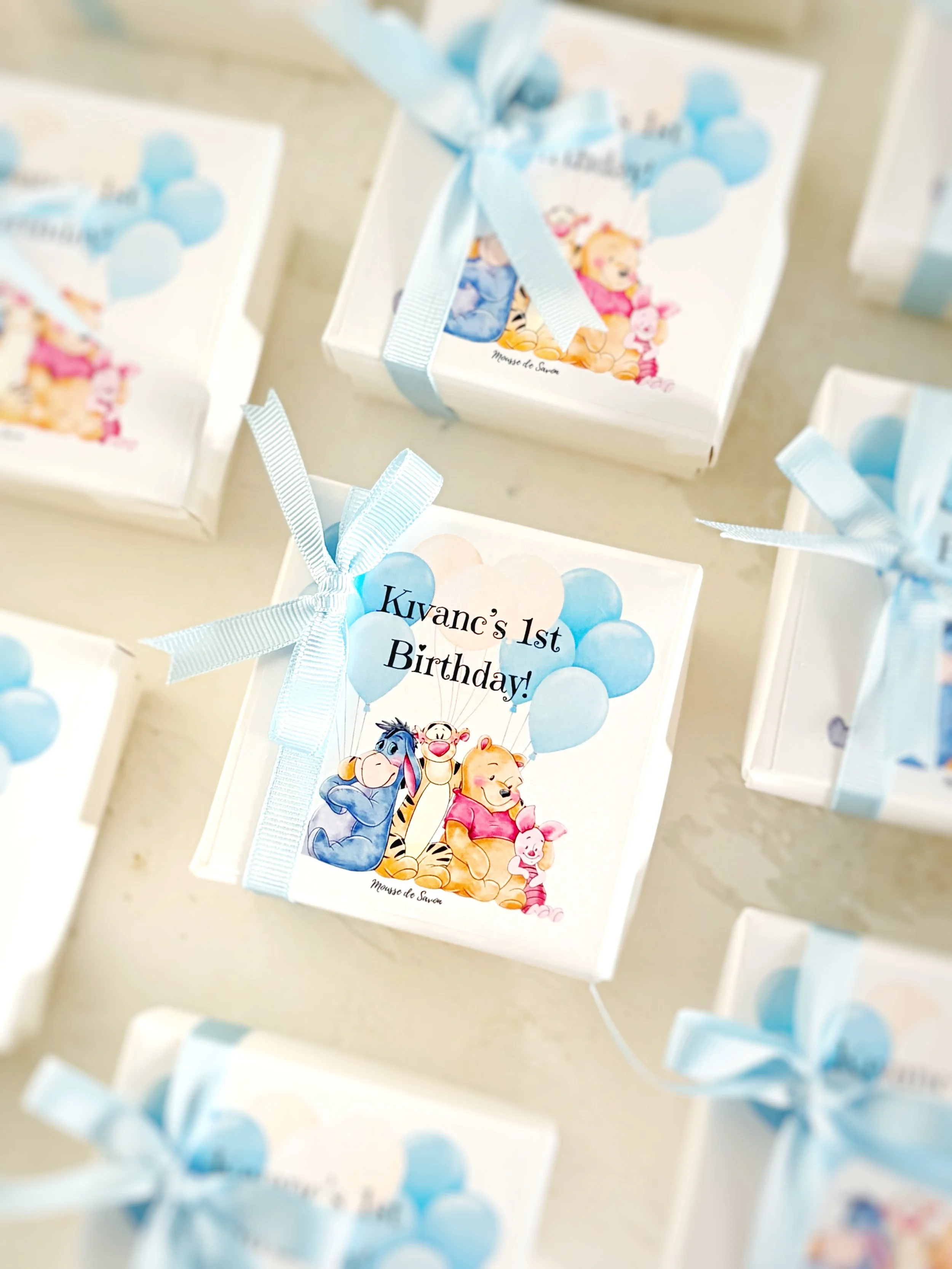 Gift box featuring Winnie the Pooh characters and balloons for Kivan's 1st birthday, wrapped with a light blue ribbon.