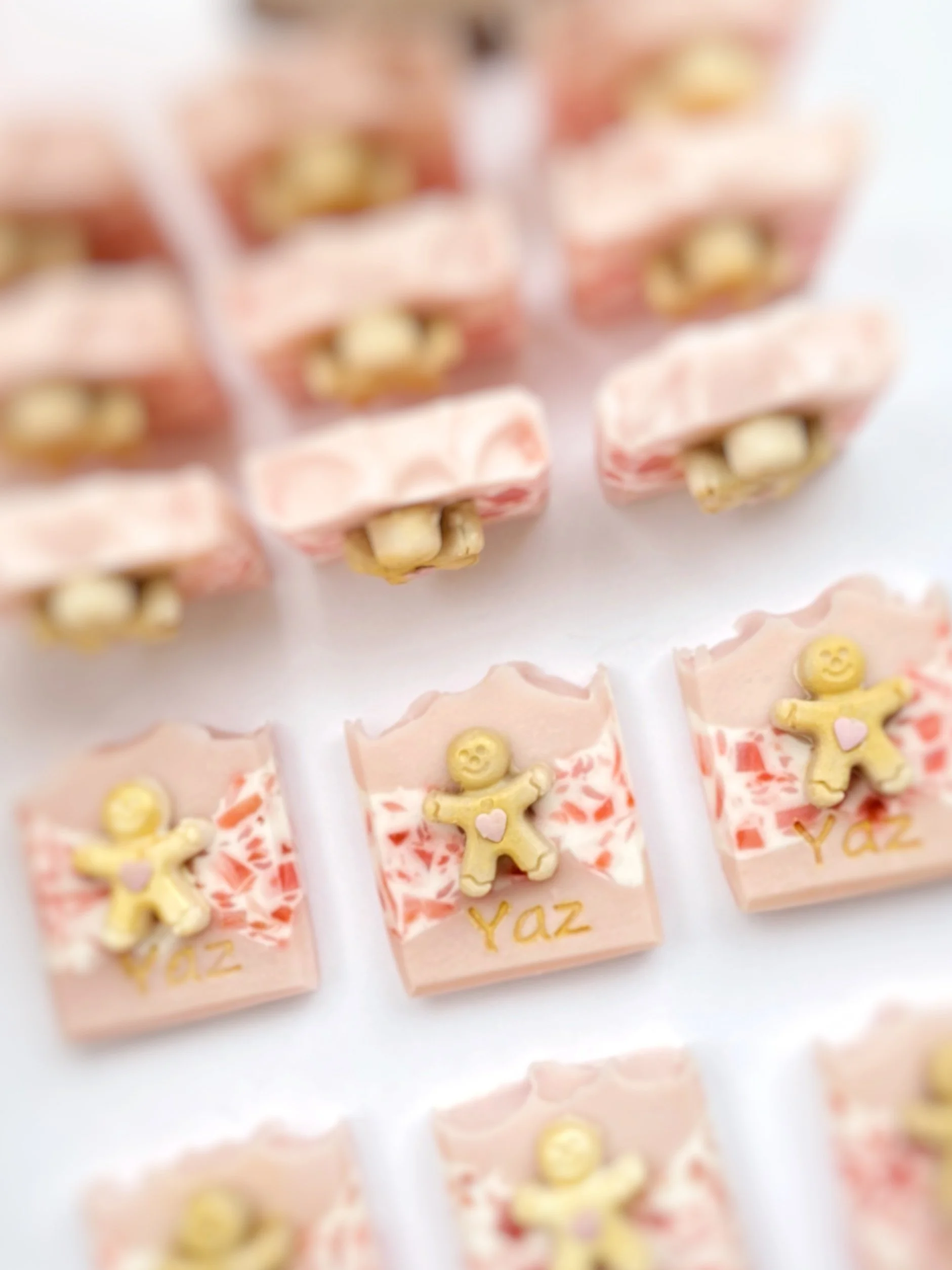 Custom pink and white decorated chocolates with a gingerbread cookie and the name Yaz, arranged on a white surface.