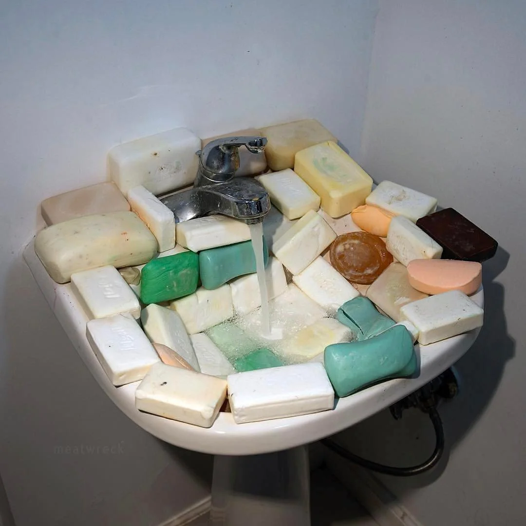 A sink filled with various bars of soap around the edges and a small amount of water in the bottom, with a silver faucet in the center.
