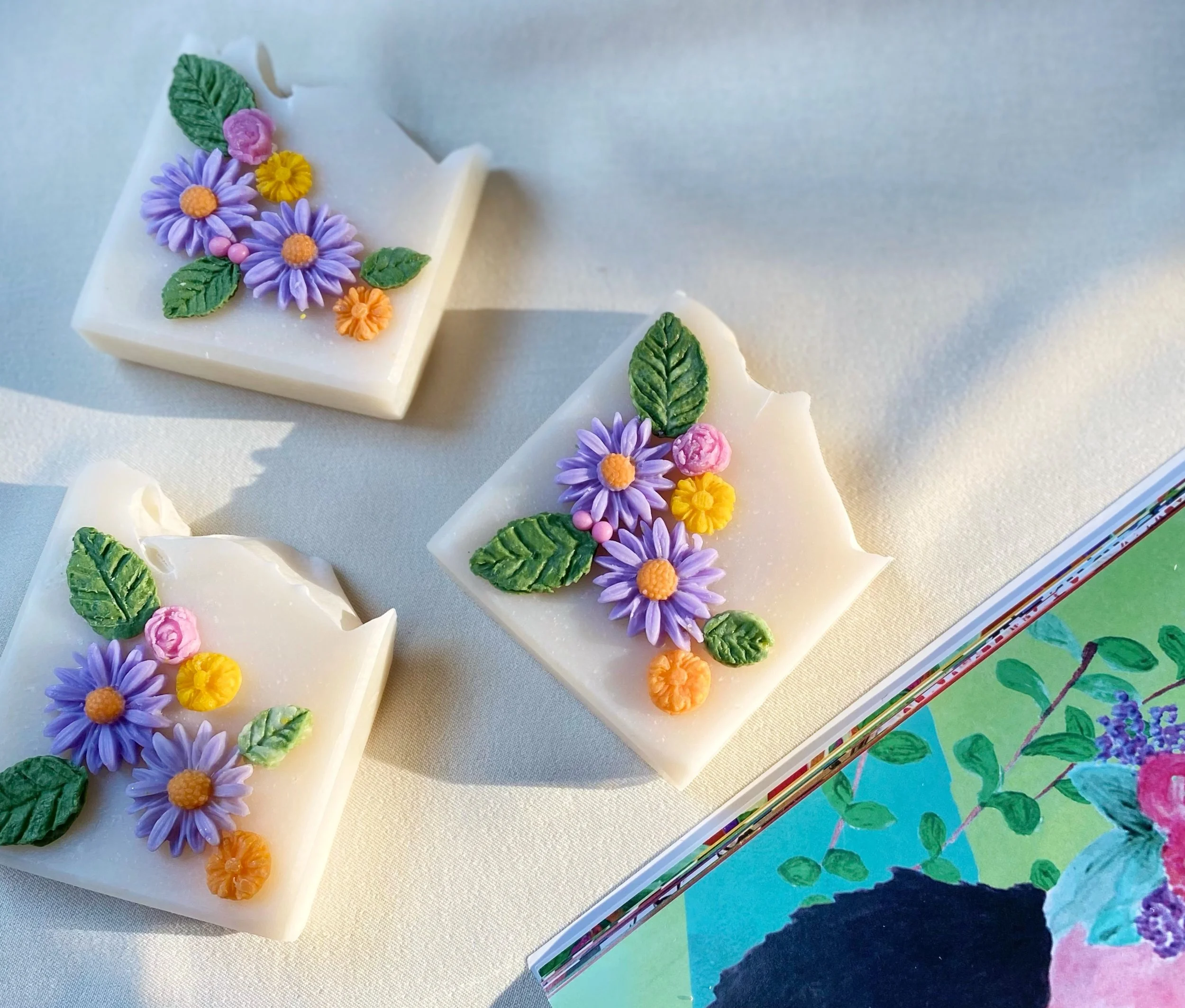 Decorative white soap bars decorated with colorful floral and leaf embellishments on a white surface.
