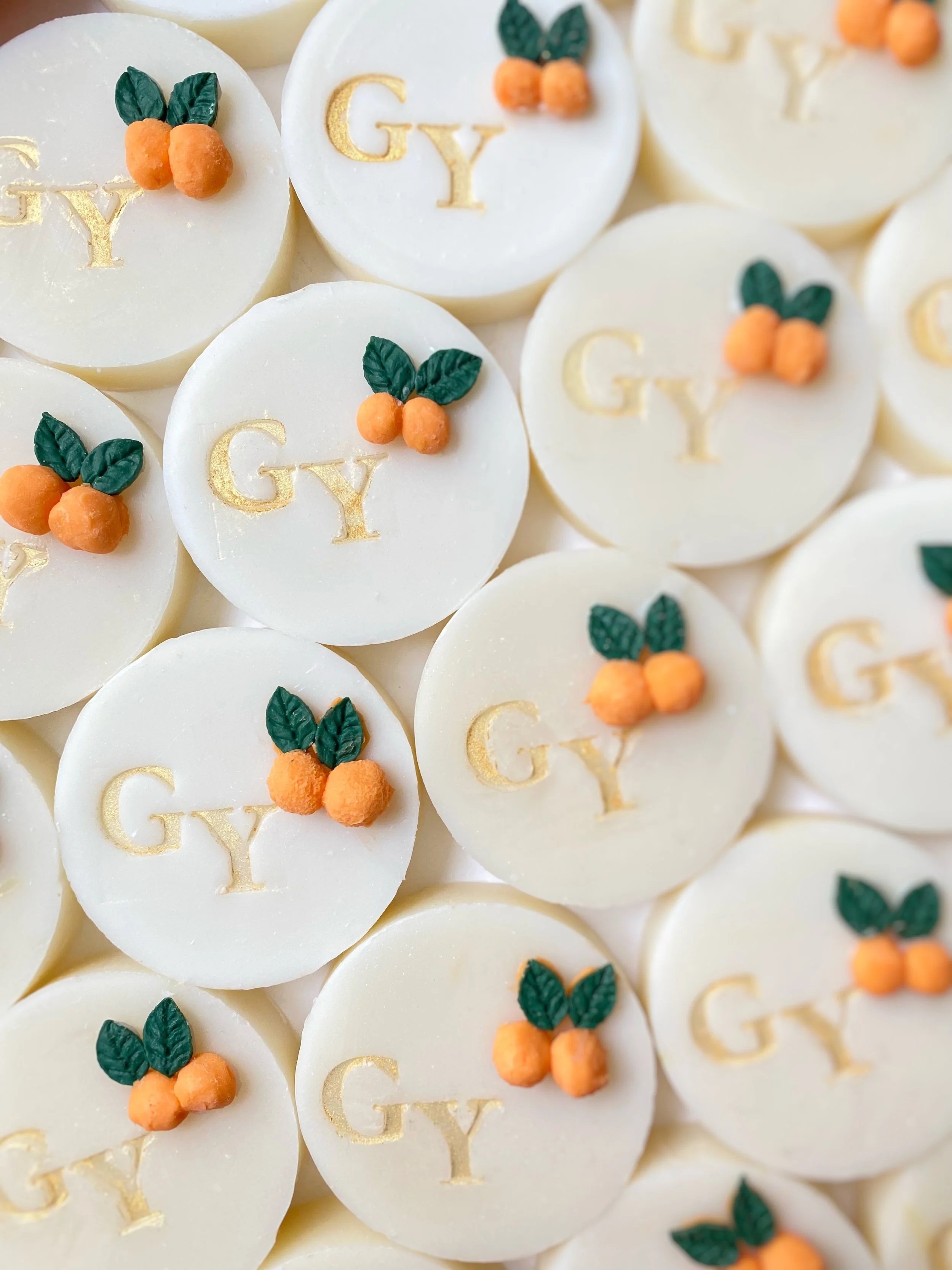 White chocolate candies with the initials "GY" in gold, decorated with small orange berries and green leaves.