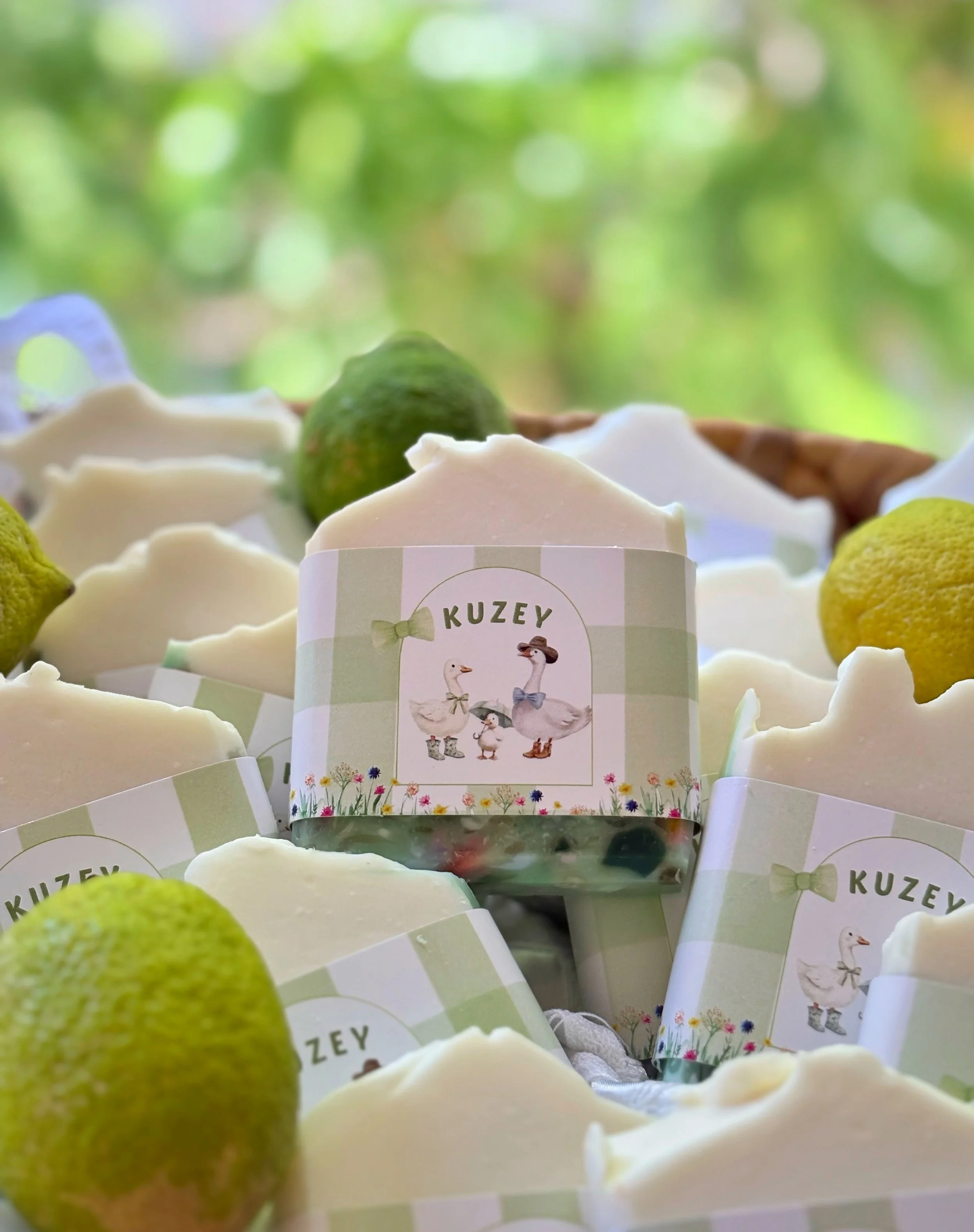 Lemon-scented candles with labels featuring cartoon ducks wearing hats, surrounded by limes and lemons, with a blurred green outdoor background.