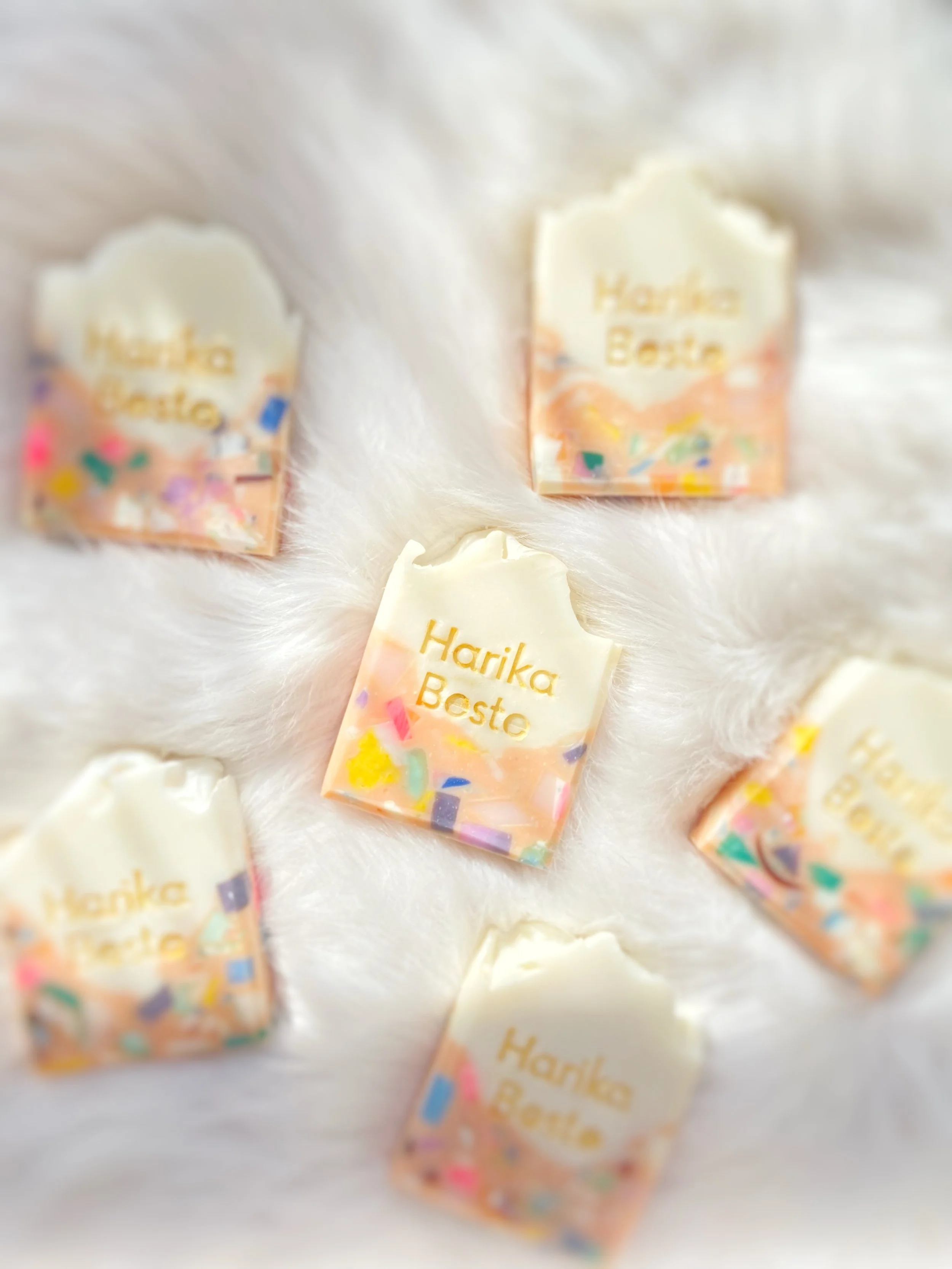 Six small rectangular chocolates with white icing, decorated with colorful sprinkles and the words 'Harika Basto' written in gold.