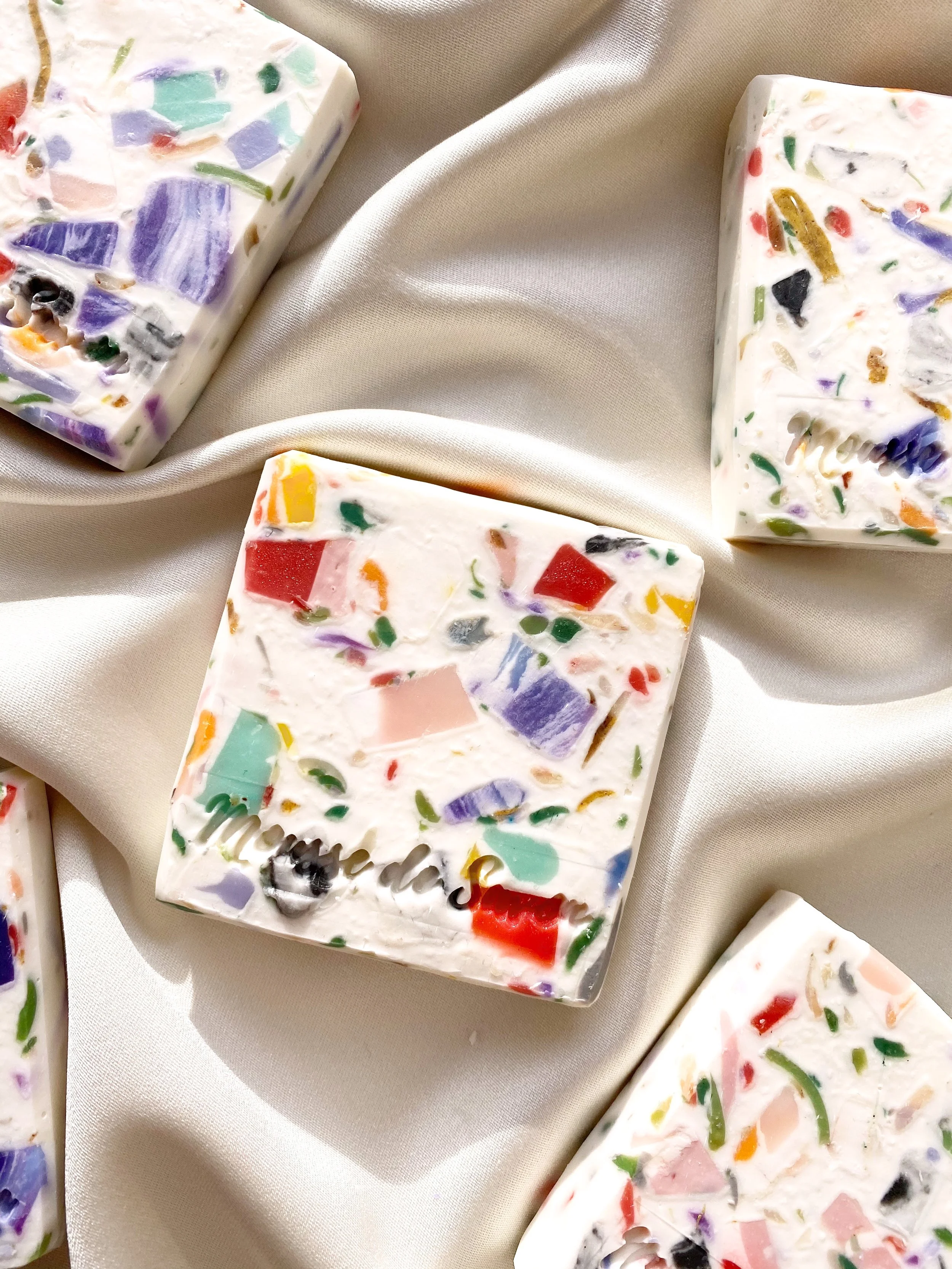 Colorful mosaic soap bars on white fabric.