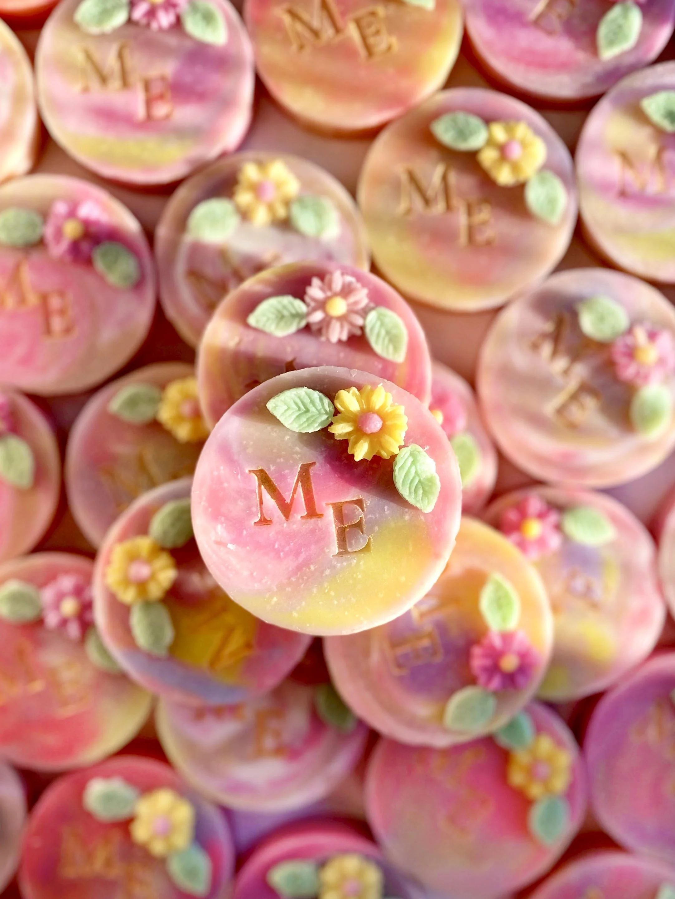 Colorful pastel candies decorated with flowers, leaves, and initials 'M E'.