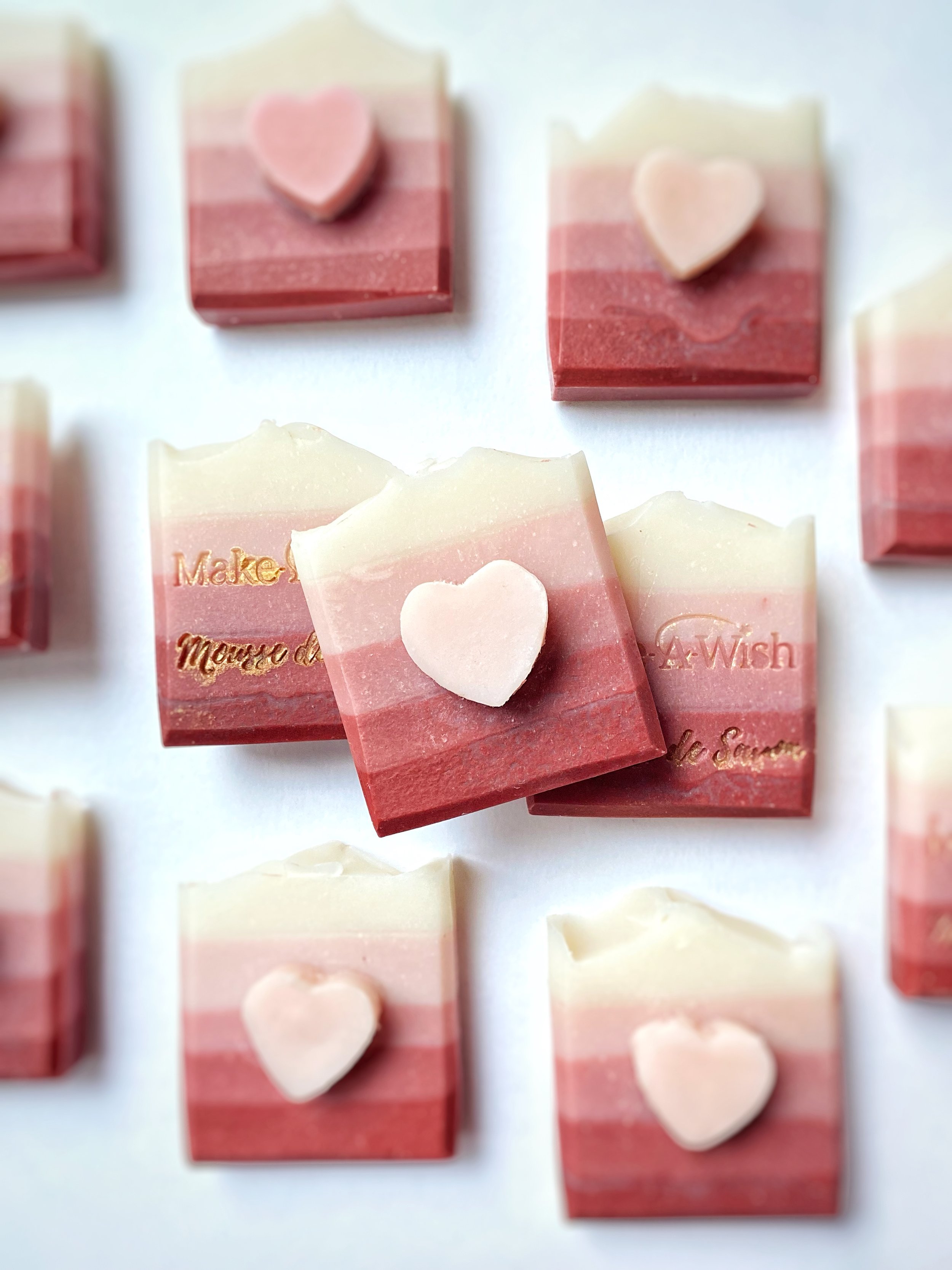 Square soap bars in pink, white, and red with a small heart shape embedded on top, arranged on a white background.