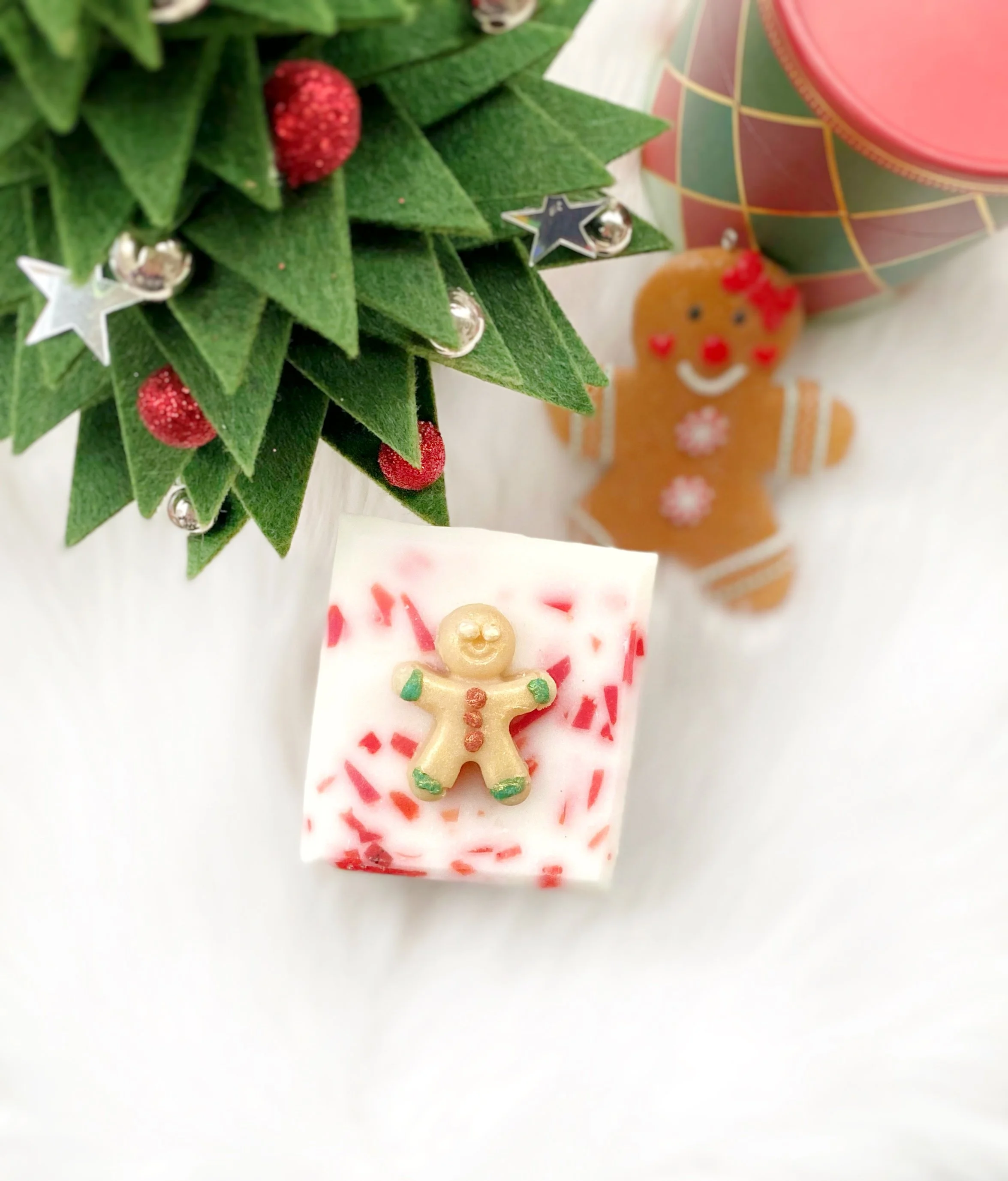 Decorative arrangement including a small felt Christmas tree with red berries and star ornaments, a gingerbread man cookie, and a white Christmas-themed soap with a gingerbread man decoration on top.
