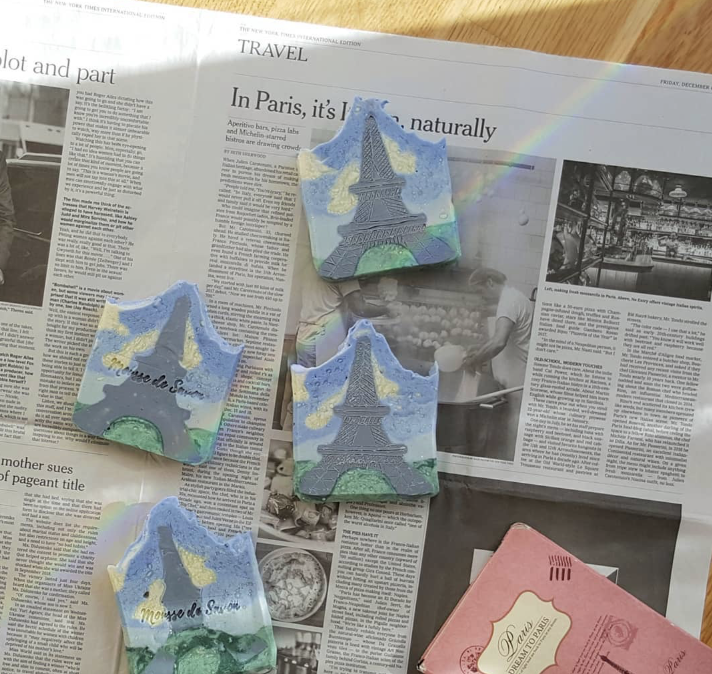 Set of four paper cutouts with the Eiffel Tower design, placed on a newspaper, with a rainbow visible in the background.