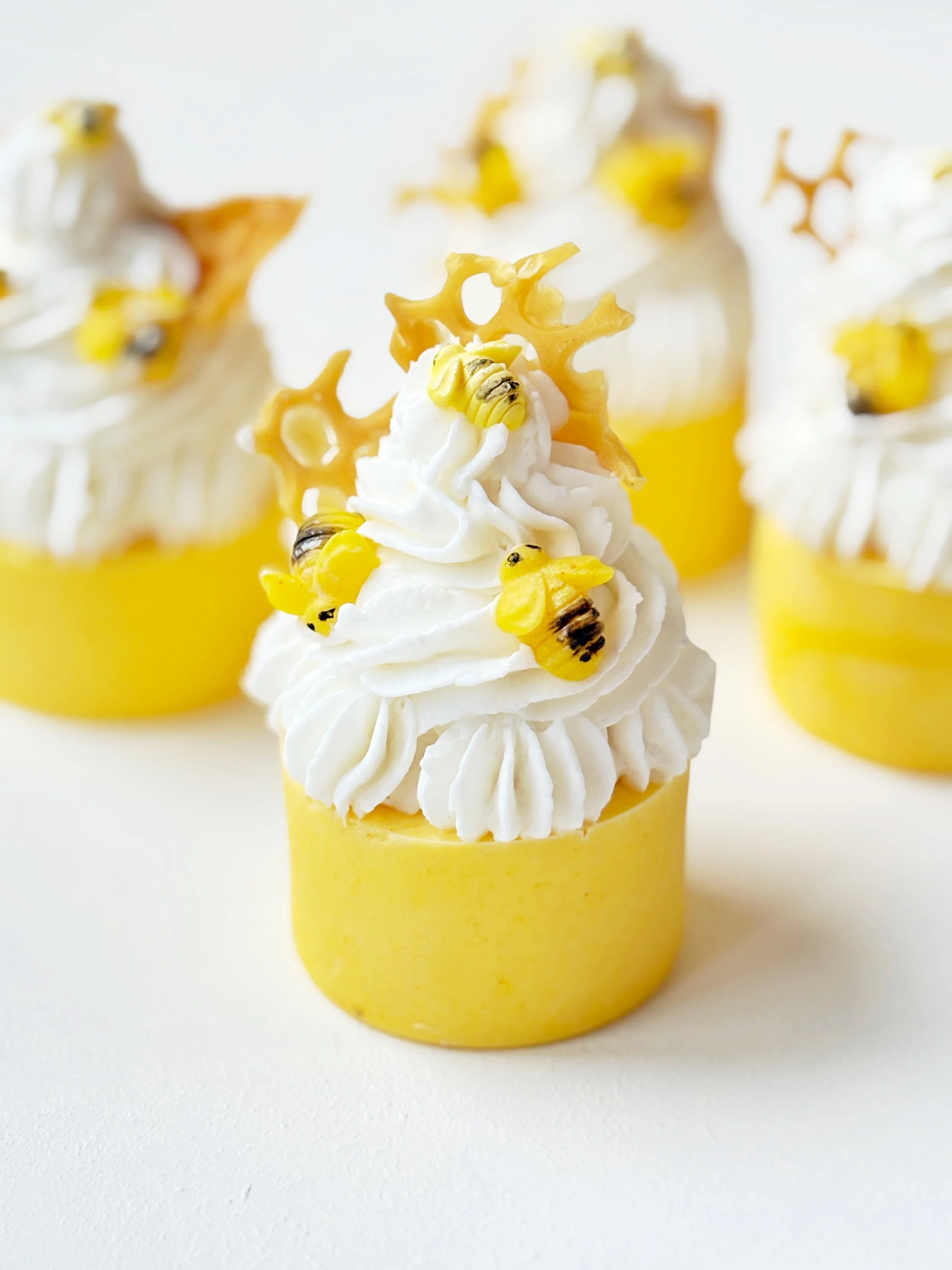 Cupcake soap with white frosting, small yellow bee decorations, and a honeycomb-shaped topper, in a yellow cupcake liner.