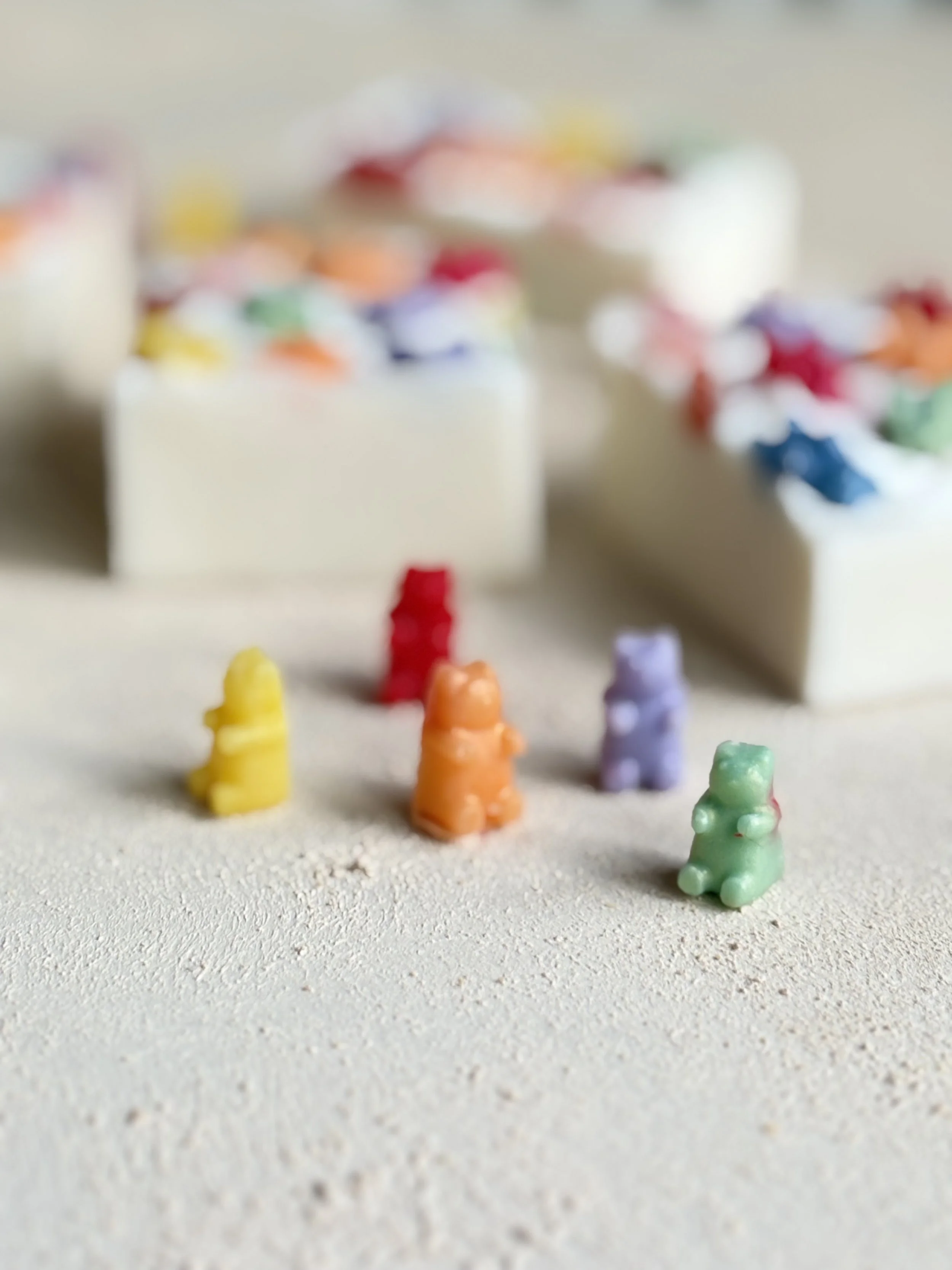 Colorful gummy bears placed on a textured surface with spilled multicolored candies in the background.