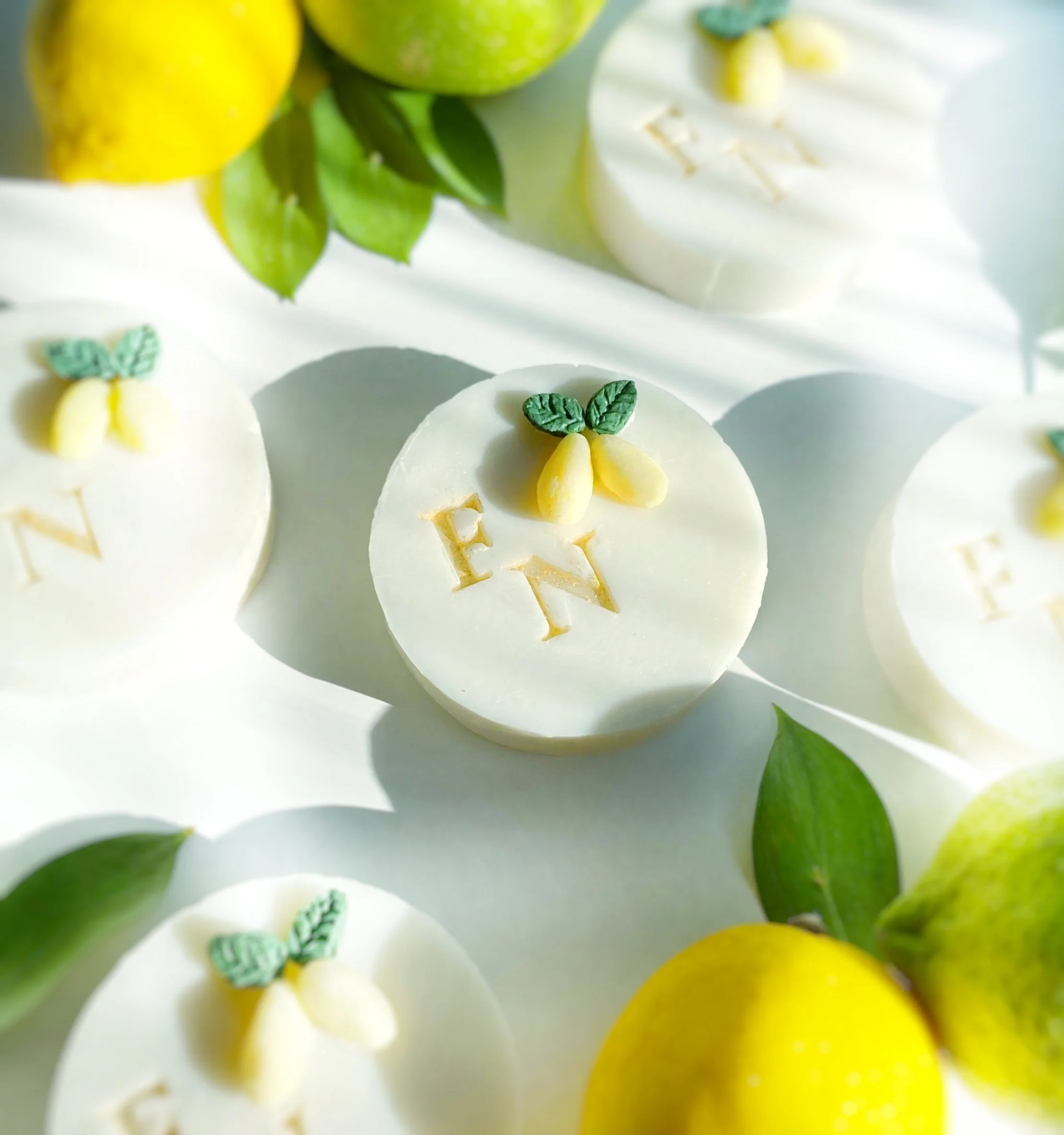 White round desserts with lemon and green leaf decorations, and the letters 'E' and 'N' on top, surrounded by lemons and green leaves.