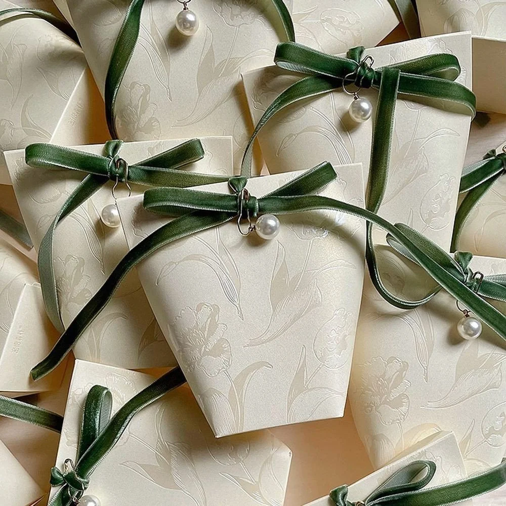 Multiple cream-colored gift boxes decorated with green satin ribbons tied in bows and large pearl ornaments.