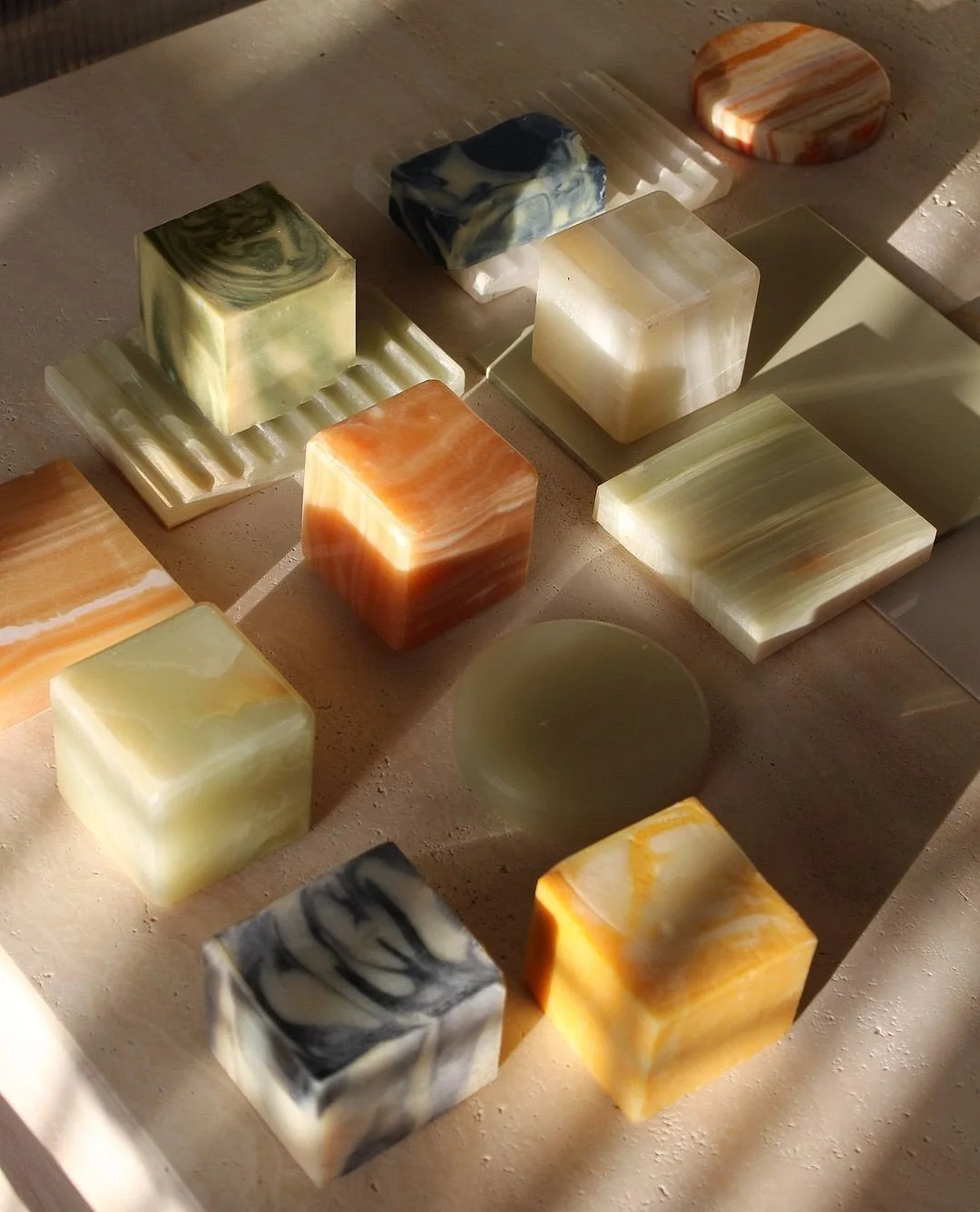 Various patterned soap bars arranged on a light-colored surface, with sunlight casting shadows.