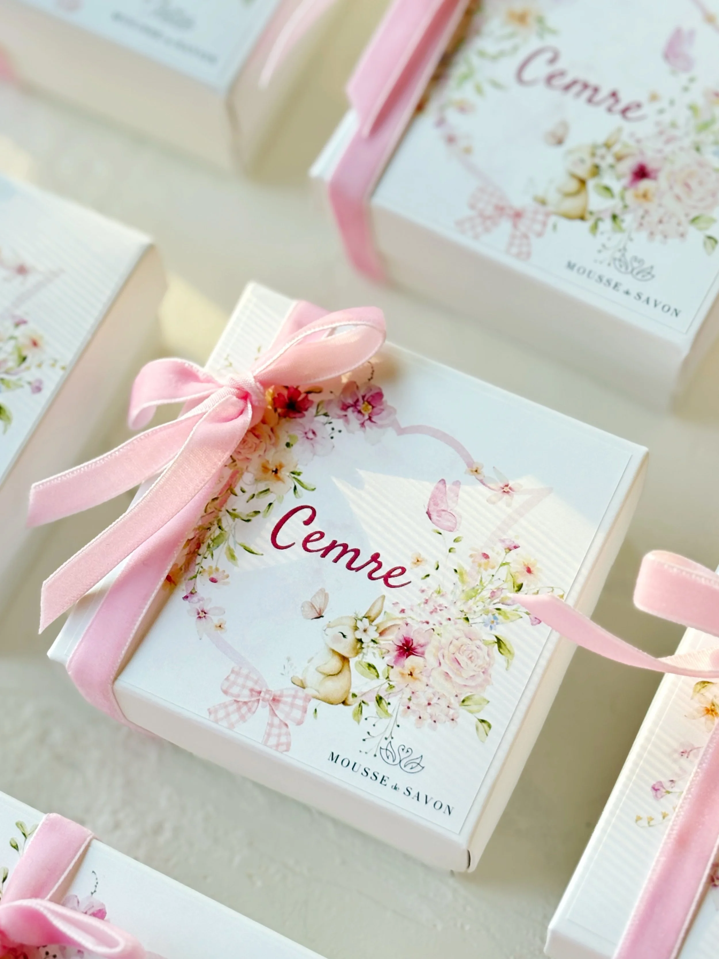 Pink gift boxes decorated with floral designs and pink ribbons, one prominently displayed with the word 'Cemre' and a rabbit illustration on the lid.
