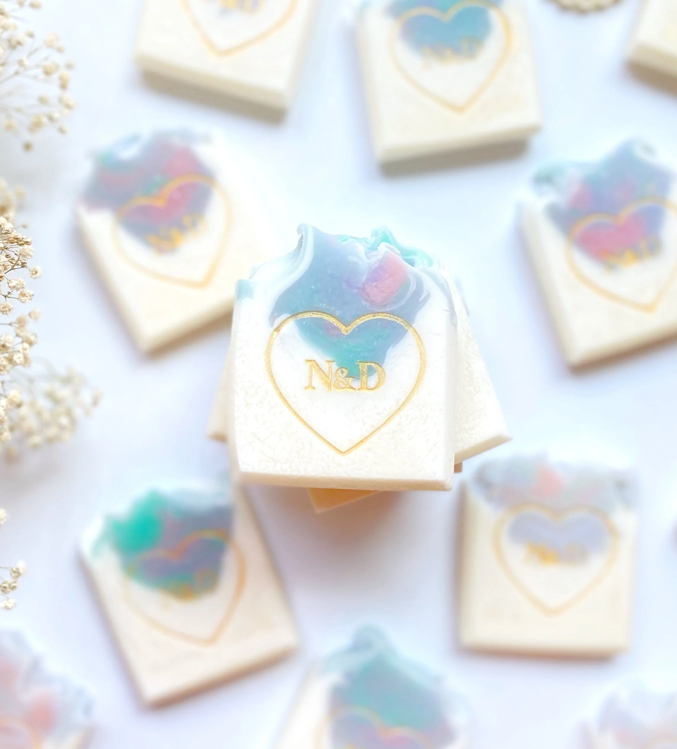 A collection of white soap bars with a heart-shaped design and the letters 'N&D' in gold, arranged on a light surface.