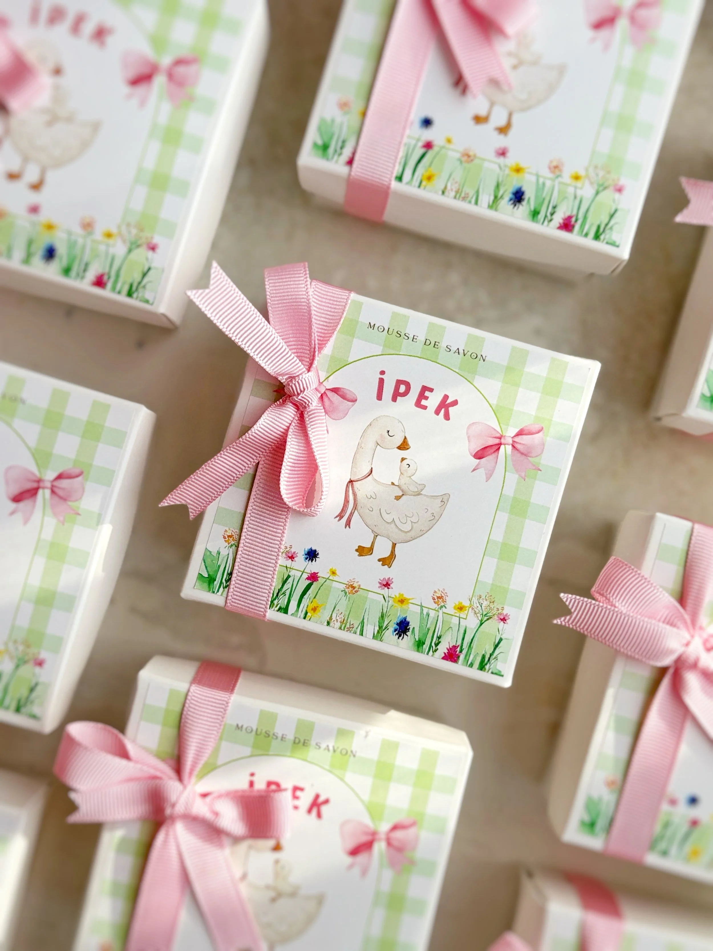 Boxes of soap with pink ribbons and a cartoon illustration of a mother goose and a duckling on the front, set on a surface.