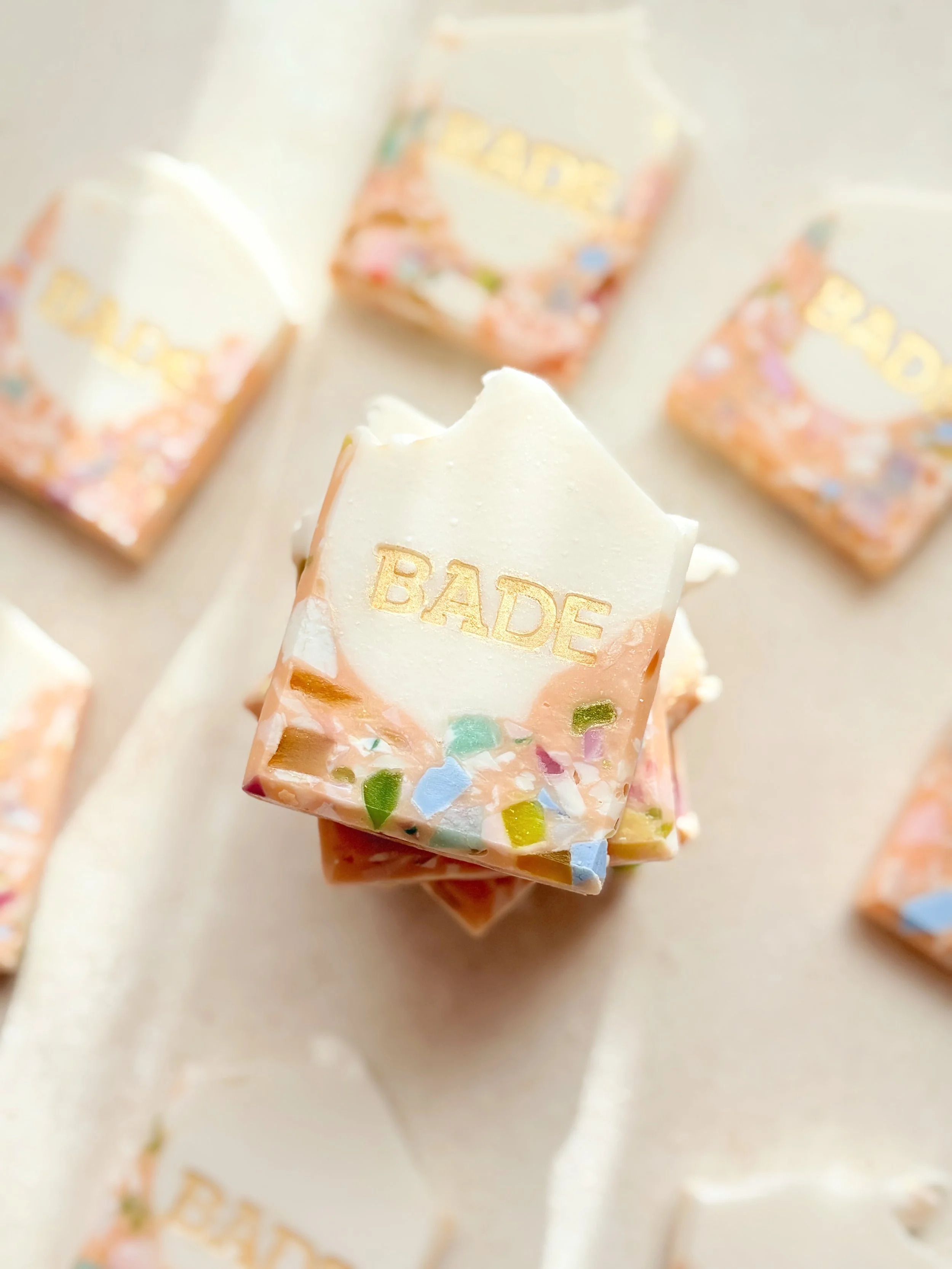 Square soap bars with multicolored sprinkles and the brand name 'BADE' engraved on the top piece, arranged on a light surface.