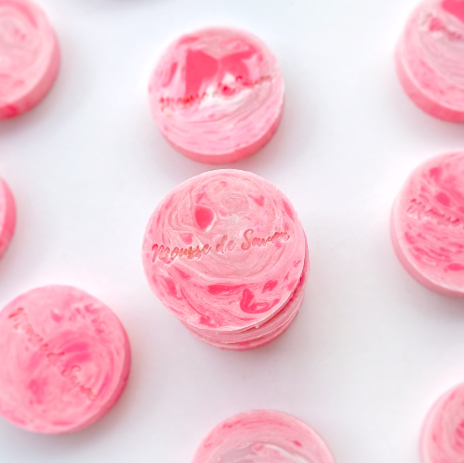 Stacked pink and white marbled soap bars with the brand name 'Maureen de Swaen' engraved on one of them, arranged on a white surface.