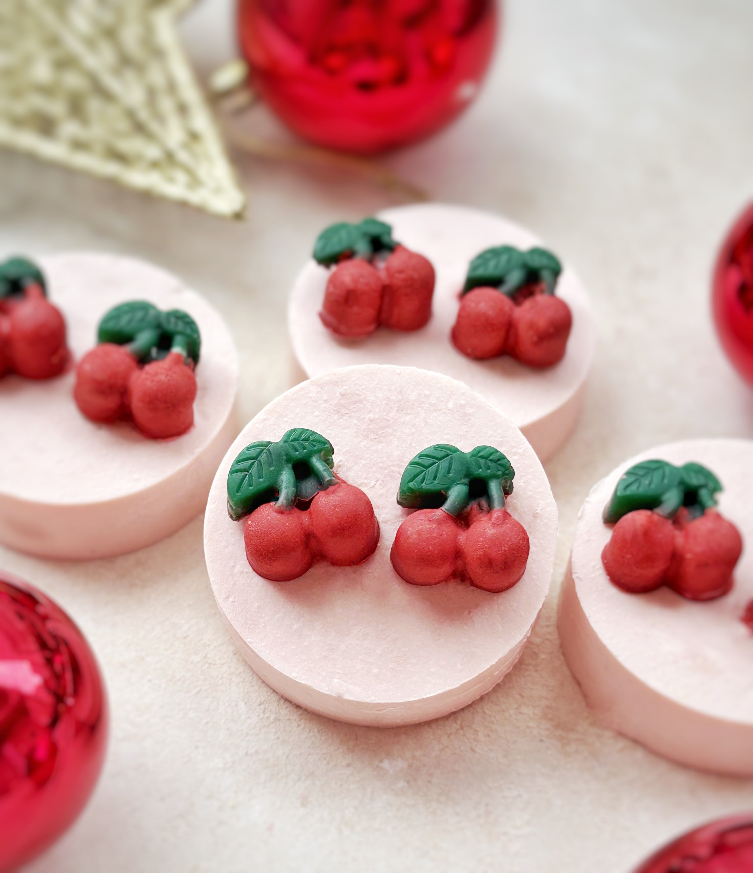 White circular bath bombs decorated with red cherry-shaped gummies with green leaves on top.