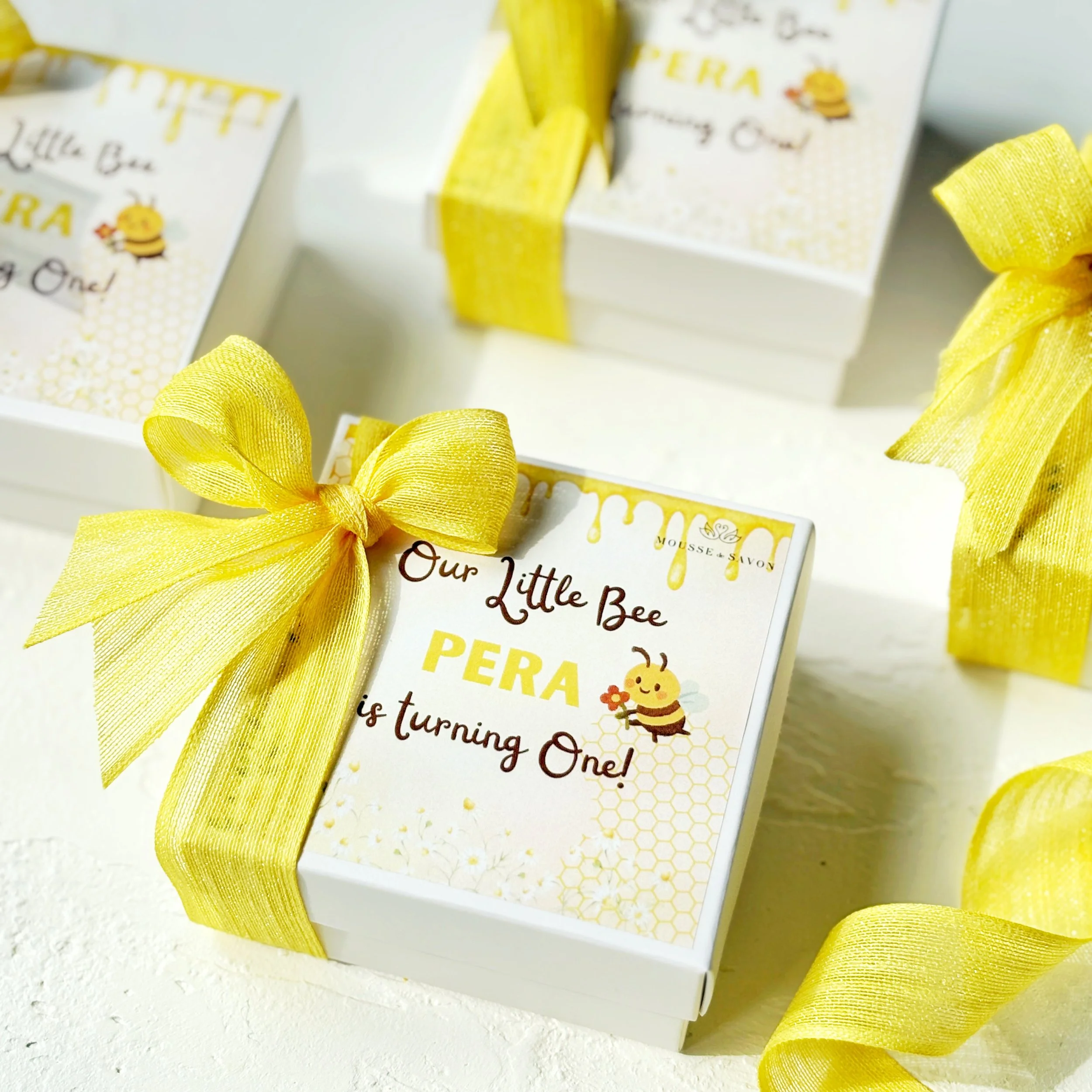 Decorative favor boxes with yellow ribbons and bee theme, celebrating a child's first birthday.