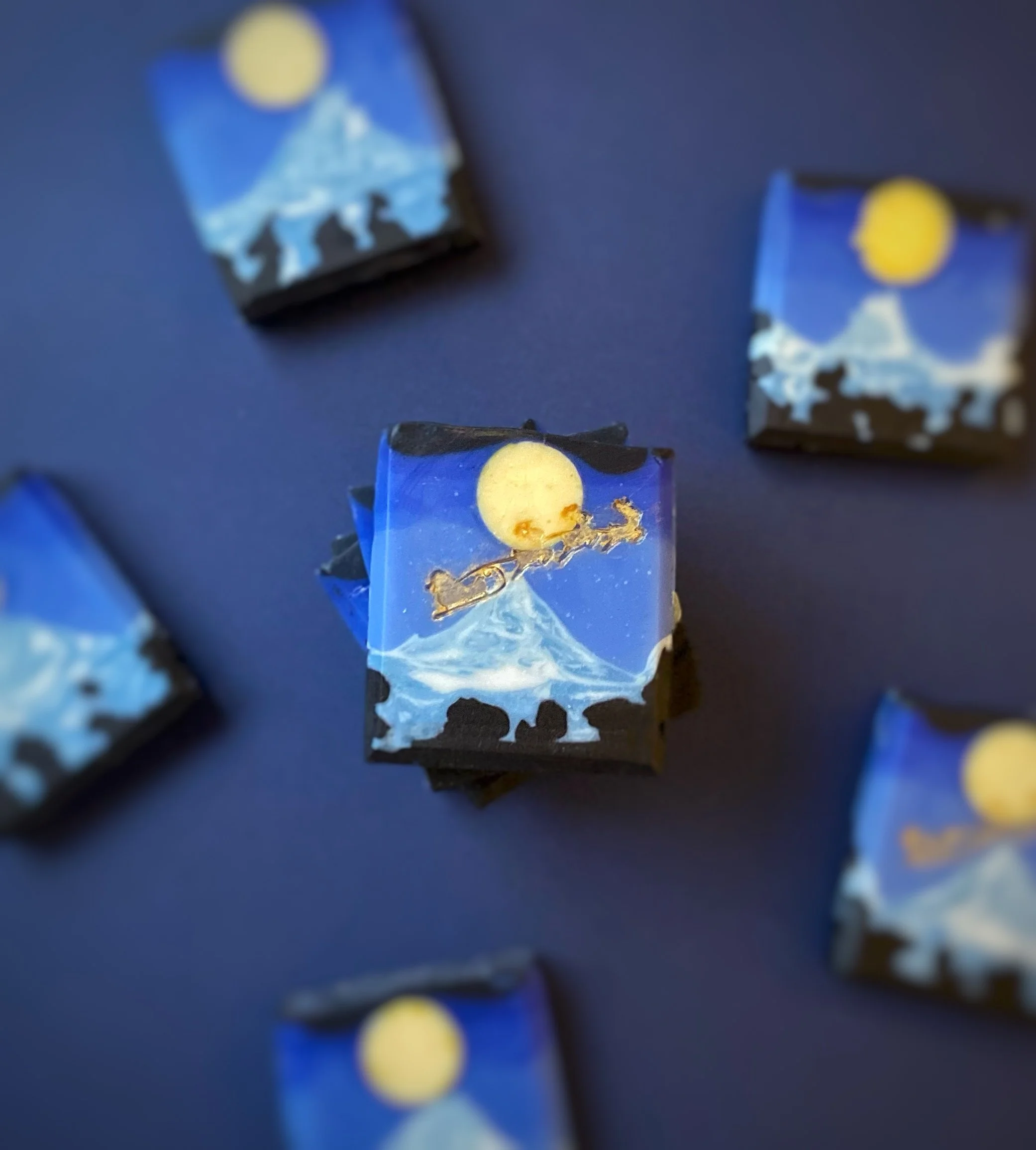 Chocolate bars decorated with mountain, moon, and night sky artwork, scattered on a dark surface.