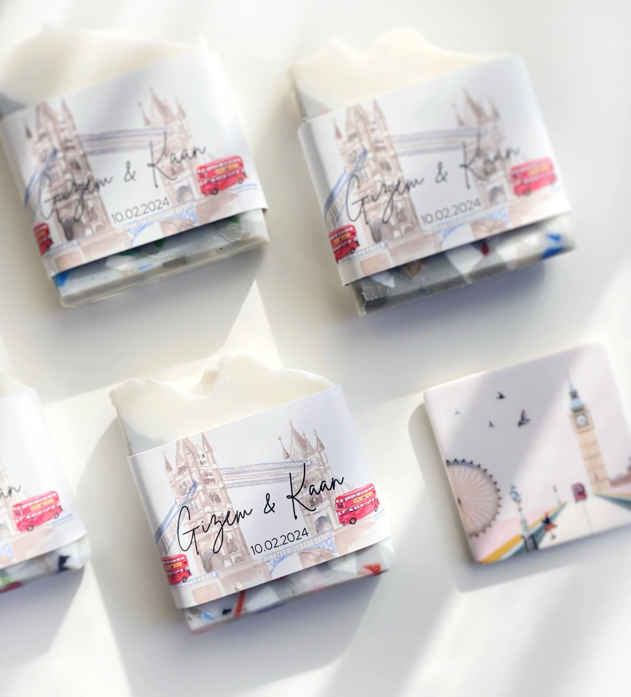Set of personalized soap bars with London-themed wrappers, featuring iconic landmarks and a red double-decker bus, with the names Gizem and Kaan and the date 10.02.2024.