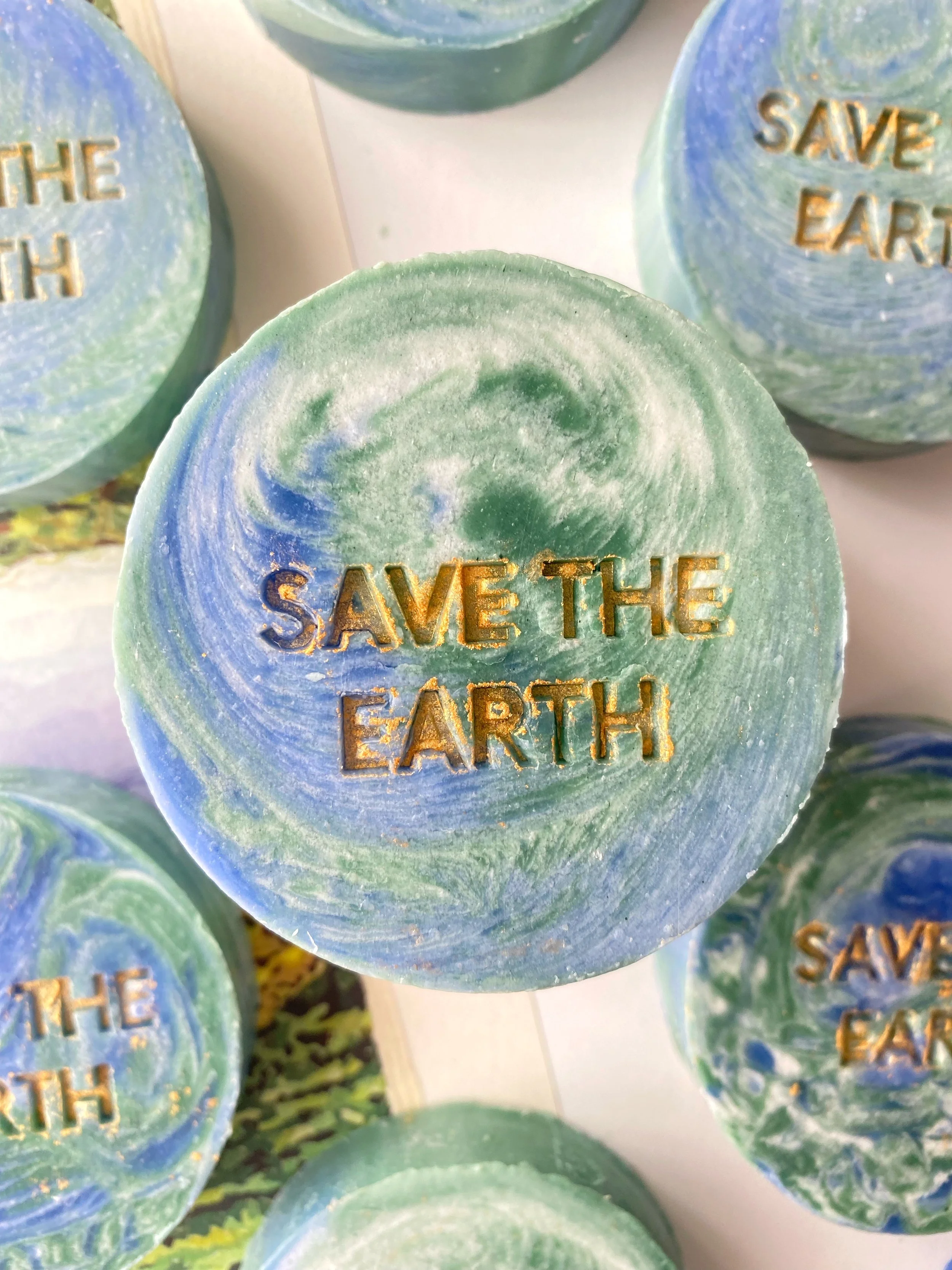 Round soaps with a swirl pattern in green and blue colors, featuring the gold embossed text 'SAVE THE EARTH' on each soap.