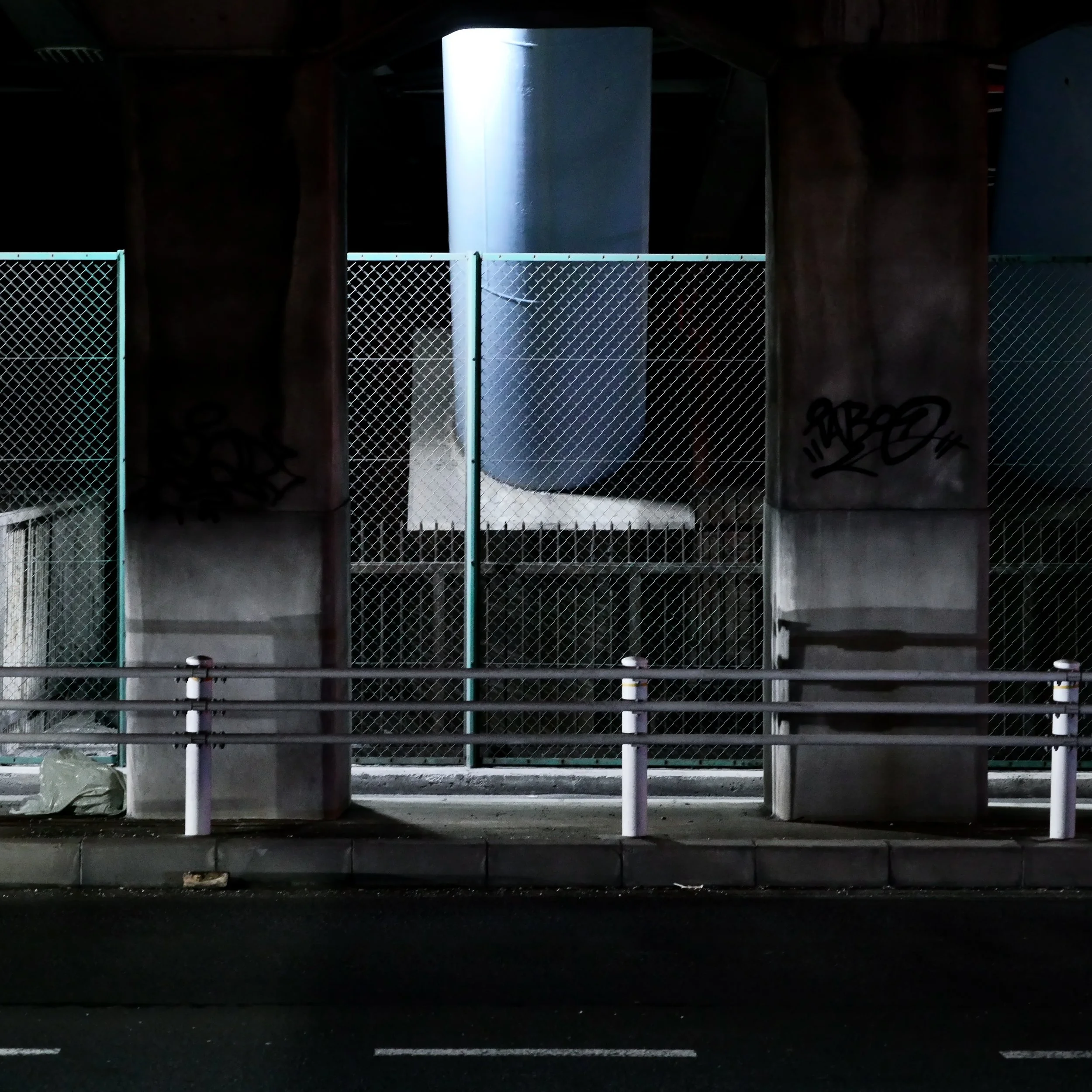 夜の都市の高架橋の柱とフェンス、下に舗装された道路が見える。