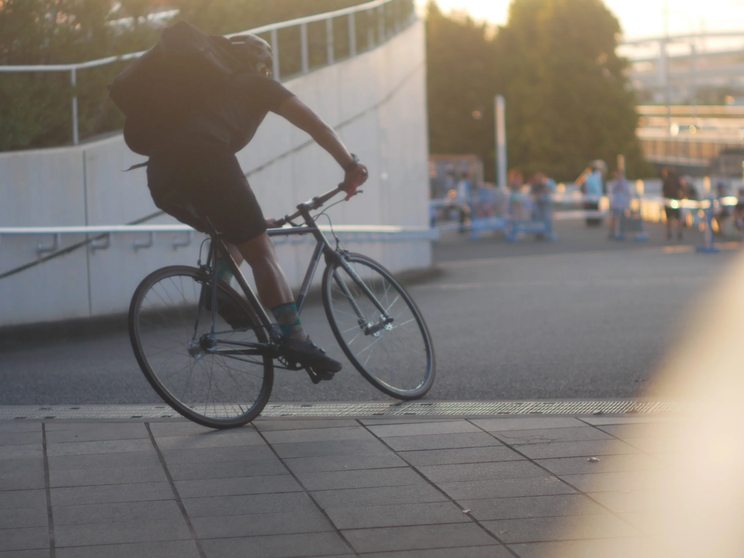 自転車に乗る男性が舗道を走っている。背景には歩いている人々と交通整理のコーンが見える。