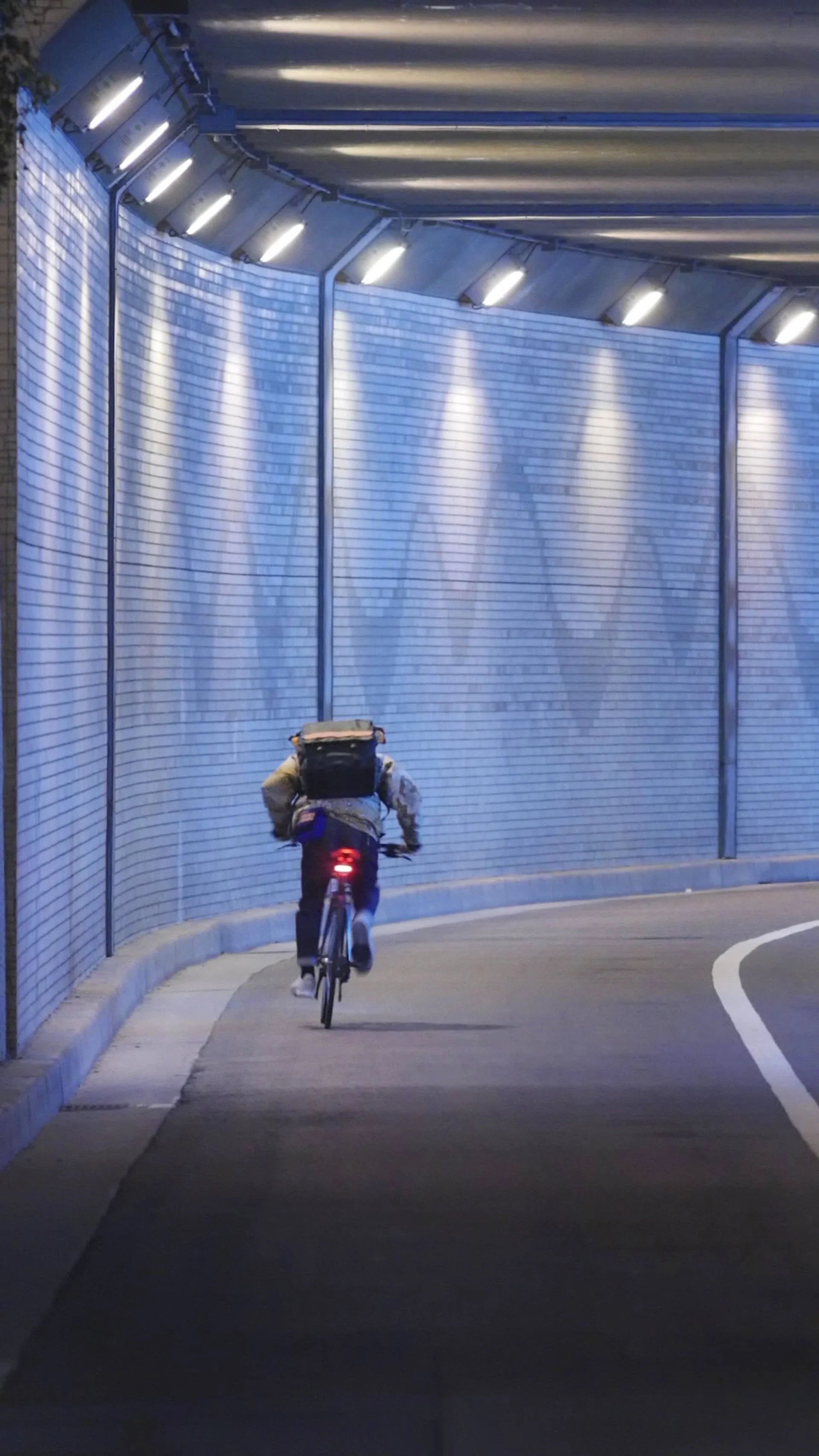 ブルーの照明が灯るトンネル内を自転車で走る人物