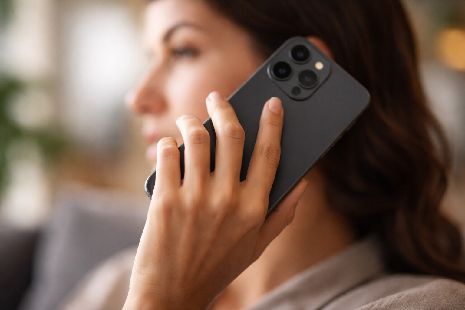 Femme tenant un smartphone noir à l'oreille, vue de profil, avec un arrière-plan flou