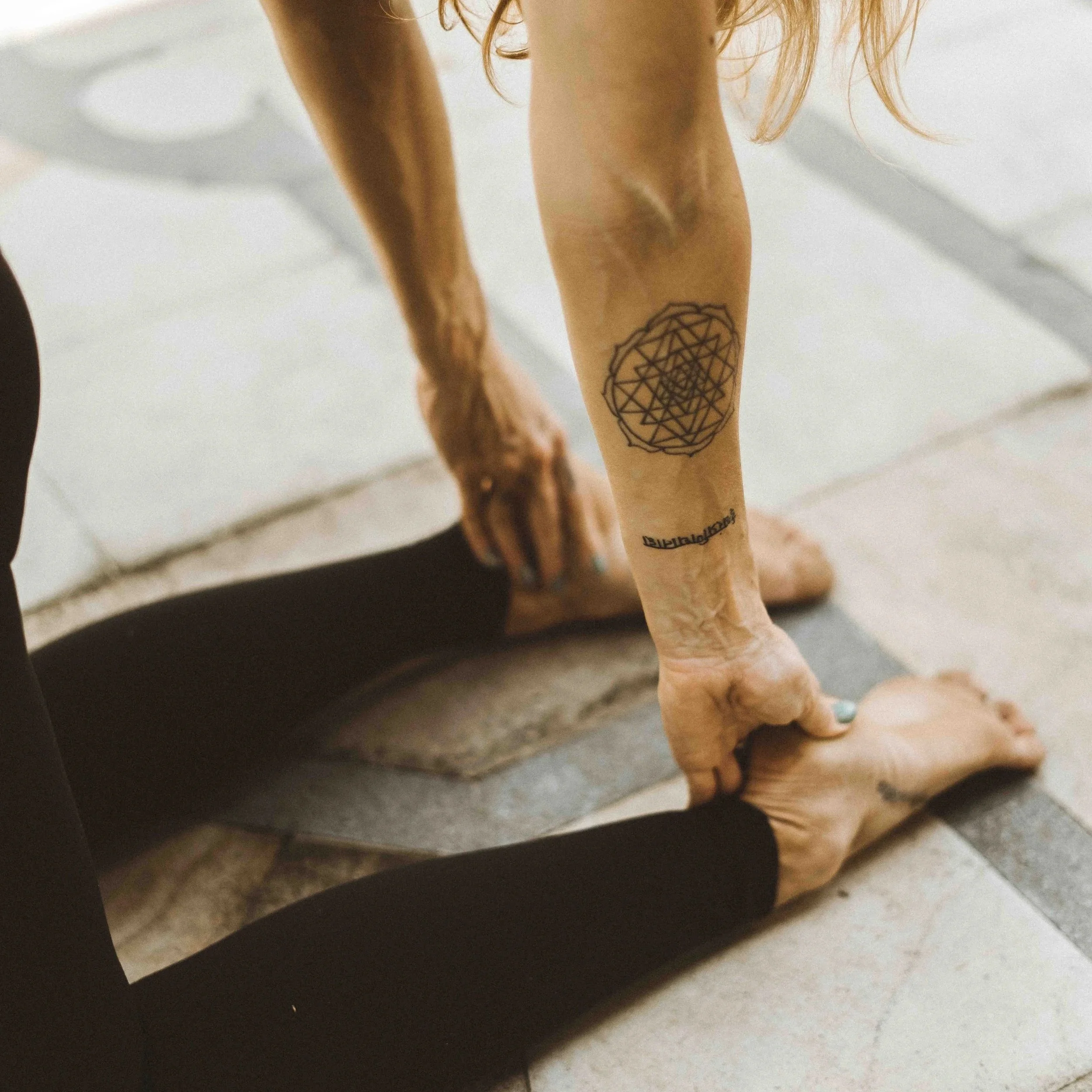A person on a yoga mat in a yoga pose with a tattoo of a geometric design on their lower leg.