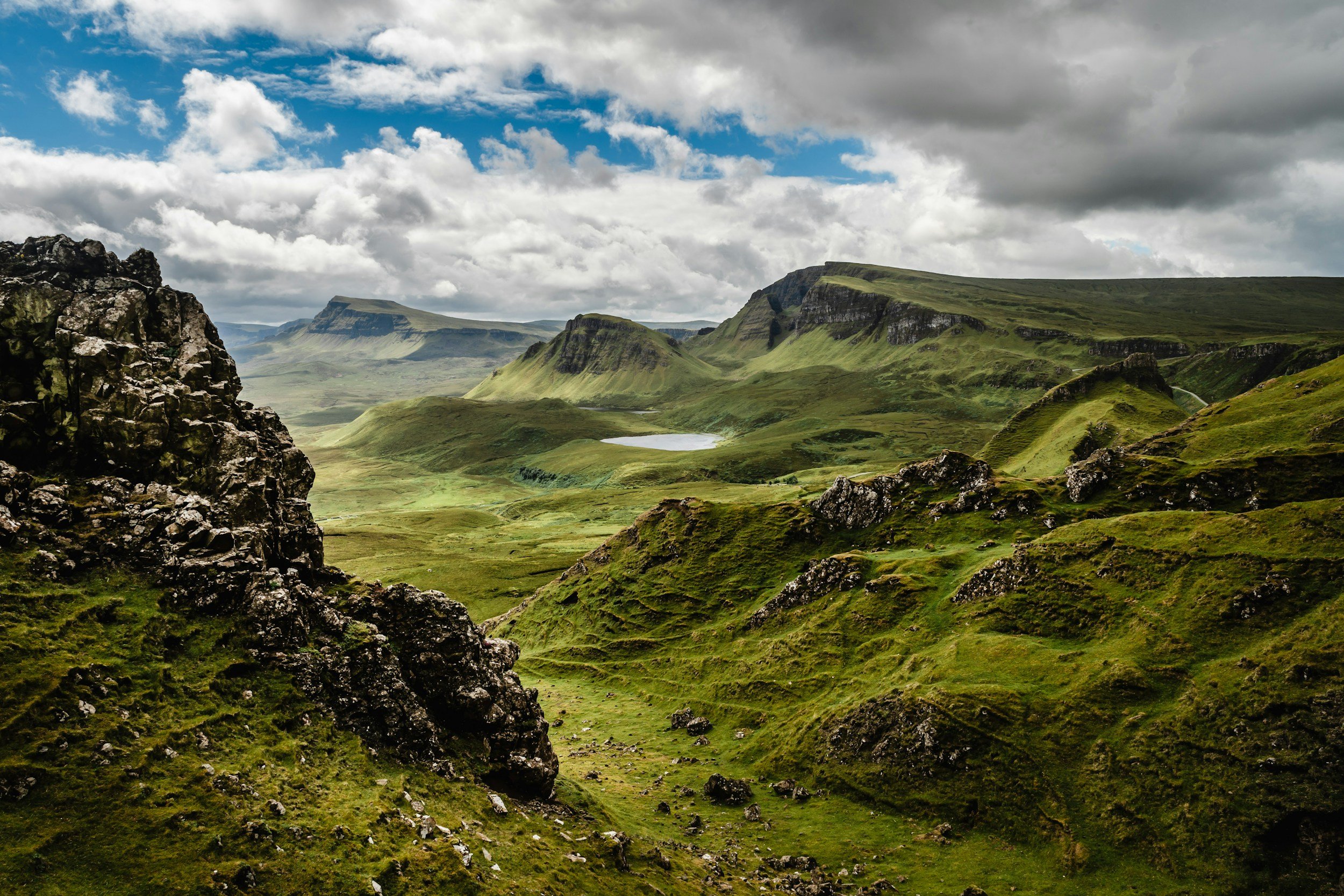 Green grassy rolling hills with rocky outcrops under a cloudy sky in a remote mountainous landscape.