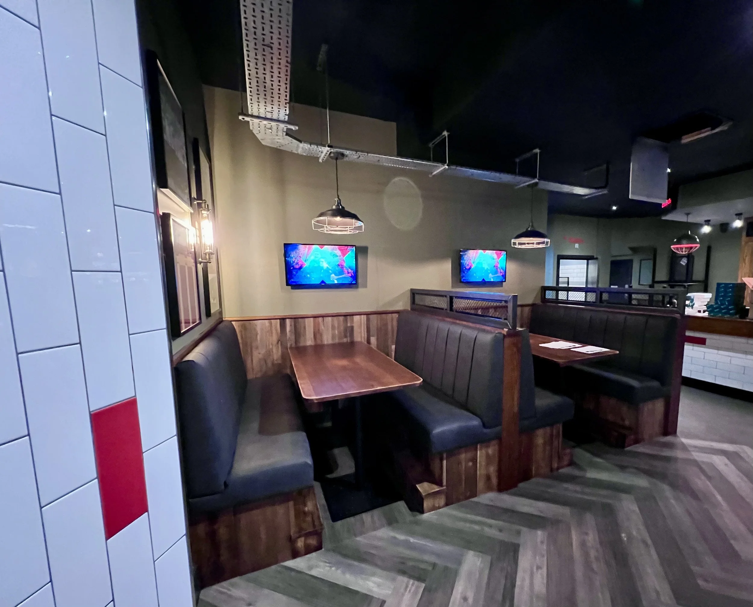 Inside a restaurant with booths, wood accents, TV screens, and dim lighting.