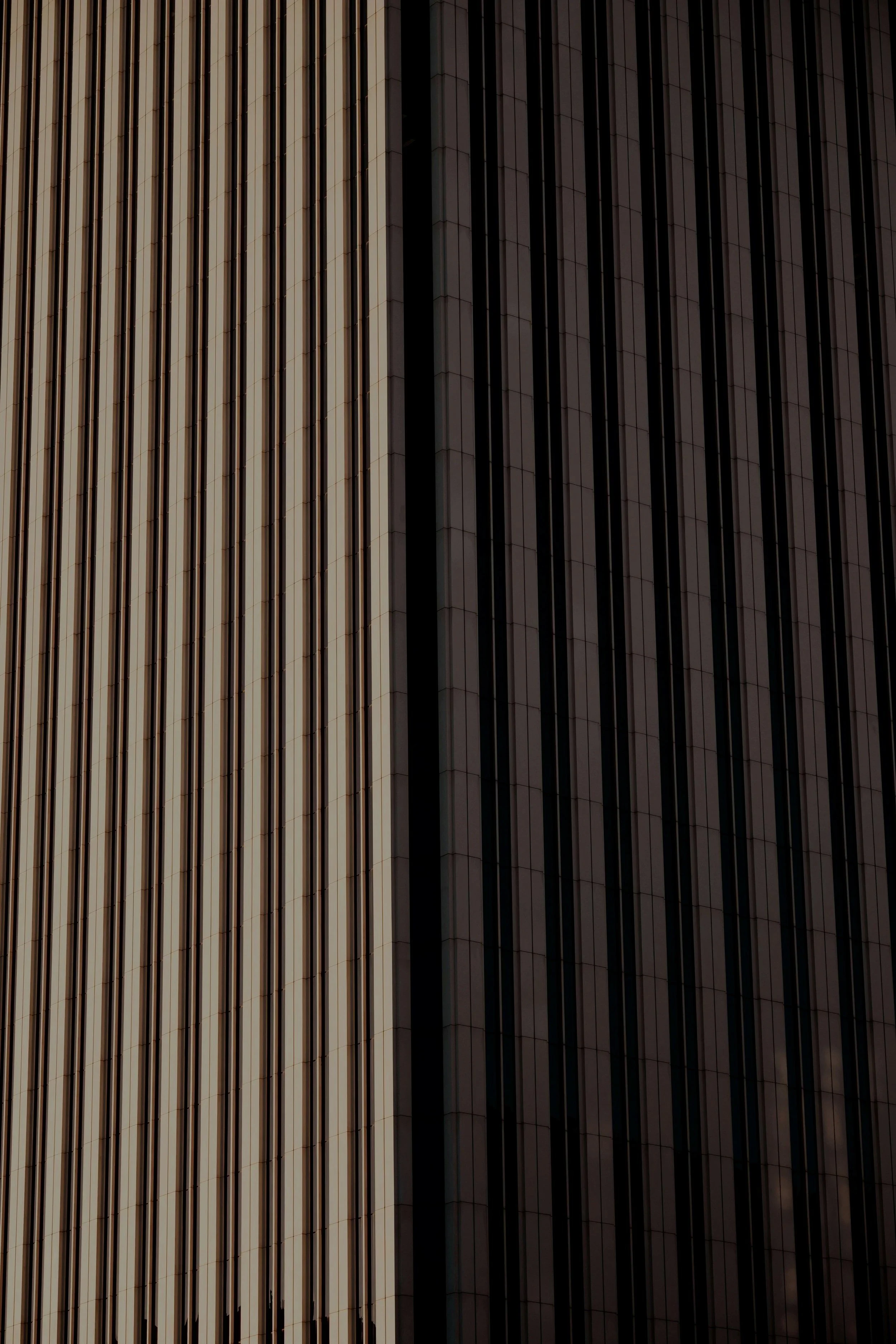 Close-up of tall building with vertical metal and glass panels, some reflecting sunlight and others in shadow.