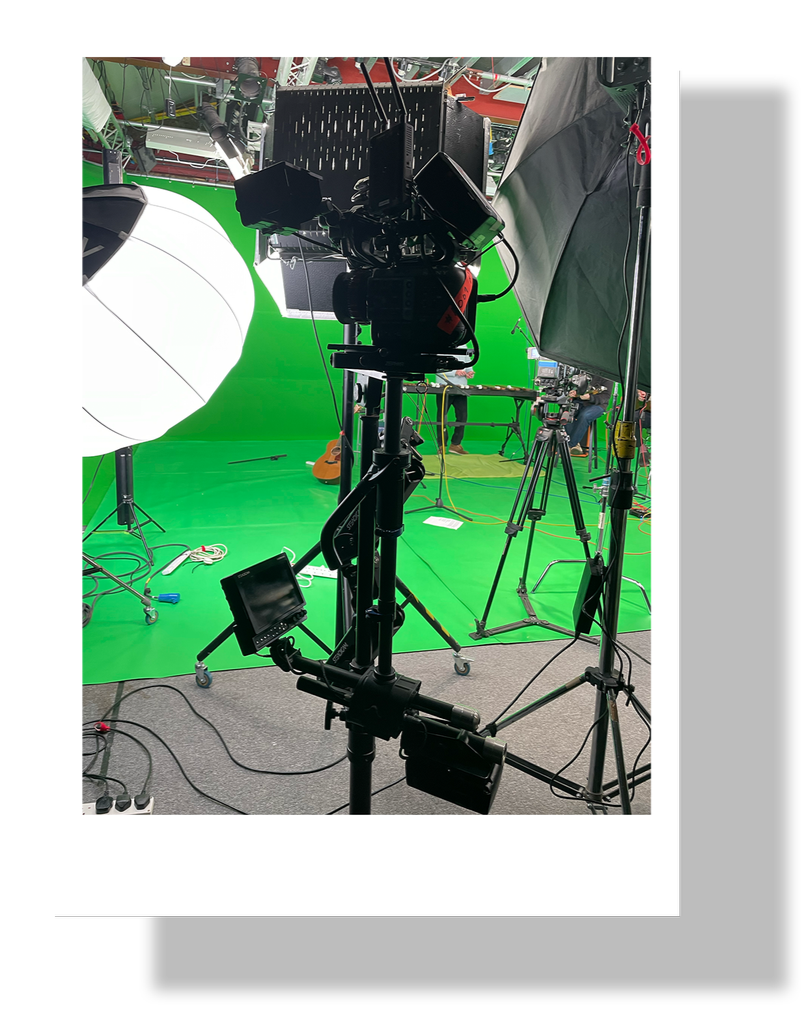 A professional video studio with a green screen backdrop, multiple cameras, lighting equipment, and a large softbox.