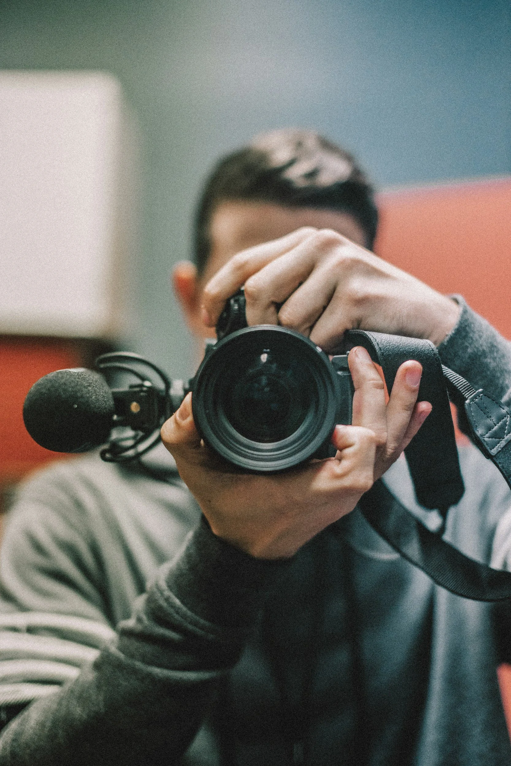 Person taking a self-portrait with a digital camera, focusing on the camera lens, in an indoor setting.