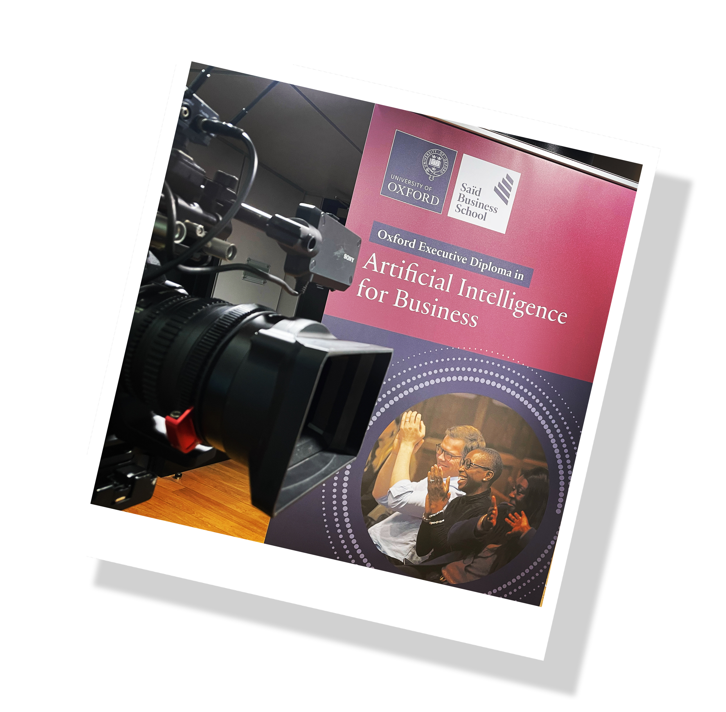 Photograph of a camera filming a promotional poster for an Oxford executive diploma in Artificial Intelligence for Business, featuring a group of smiling people clapping.
