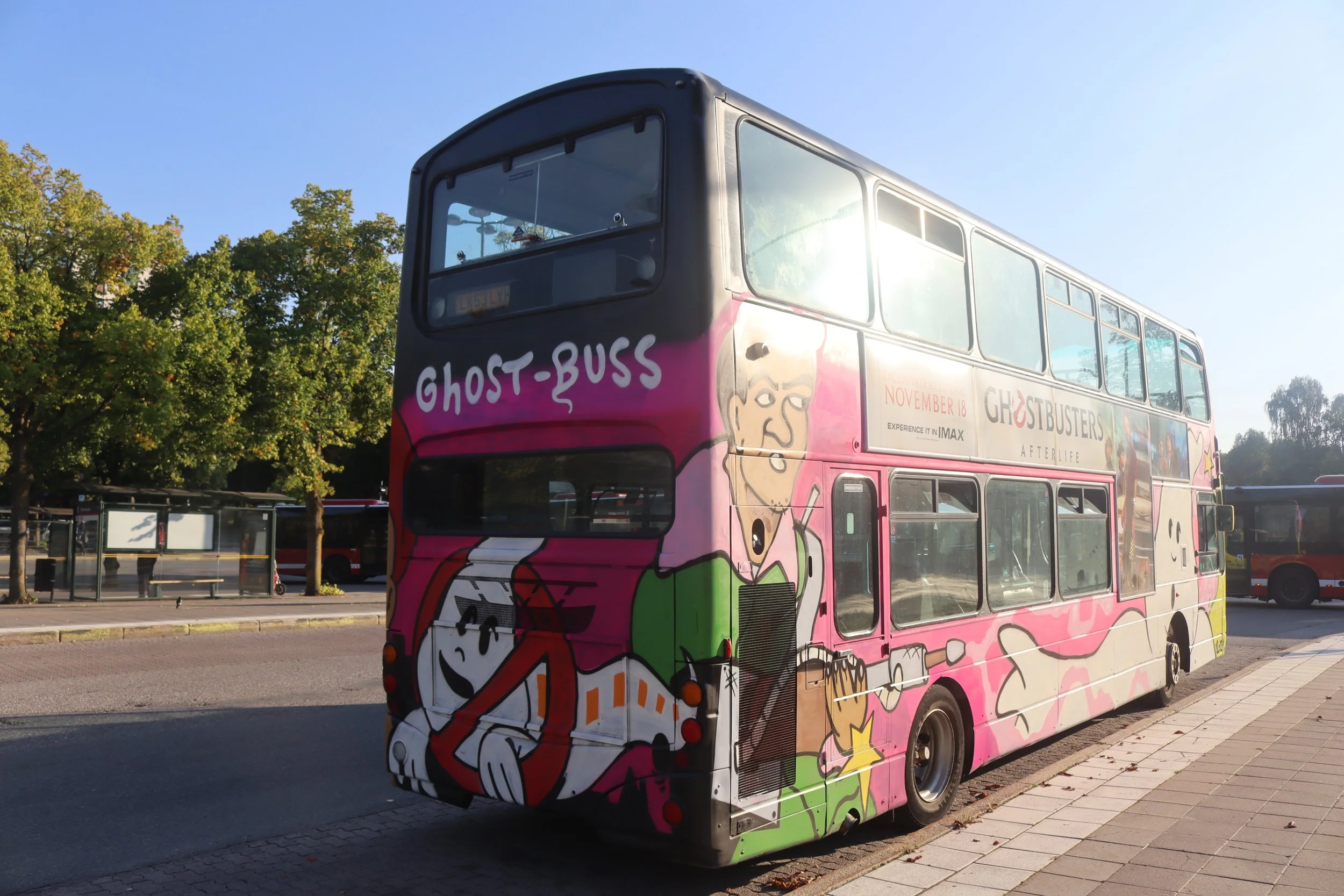 Double-decker bus painted with Ghostbusters-themed artwork, including characters and logo, parked on the side of the street.