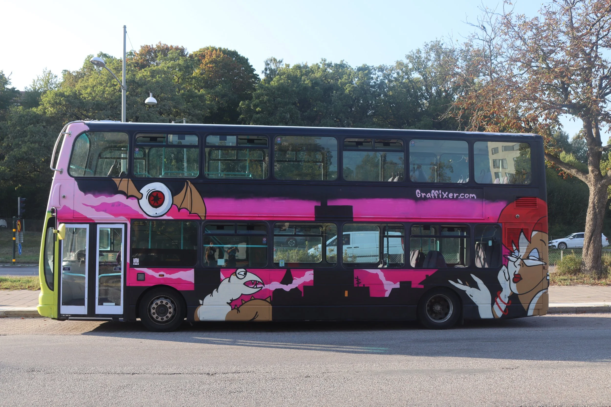 Double-decker bus with a pink and black graffiti art design featuring cartoon bats and a stylized woman with glasses and red lipstick.