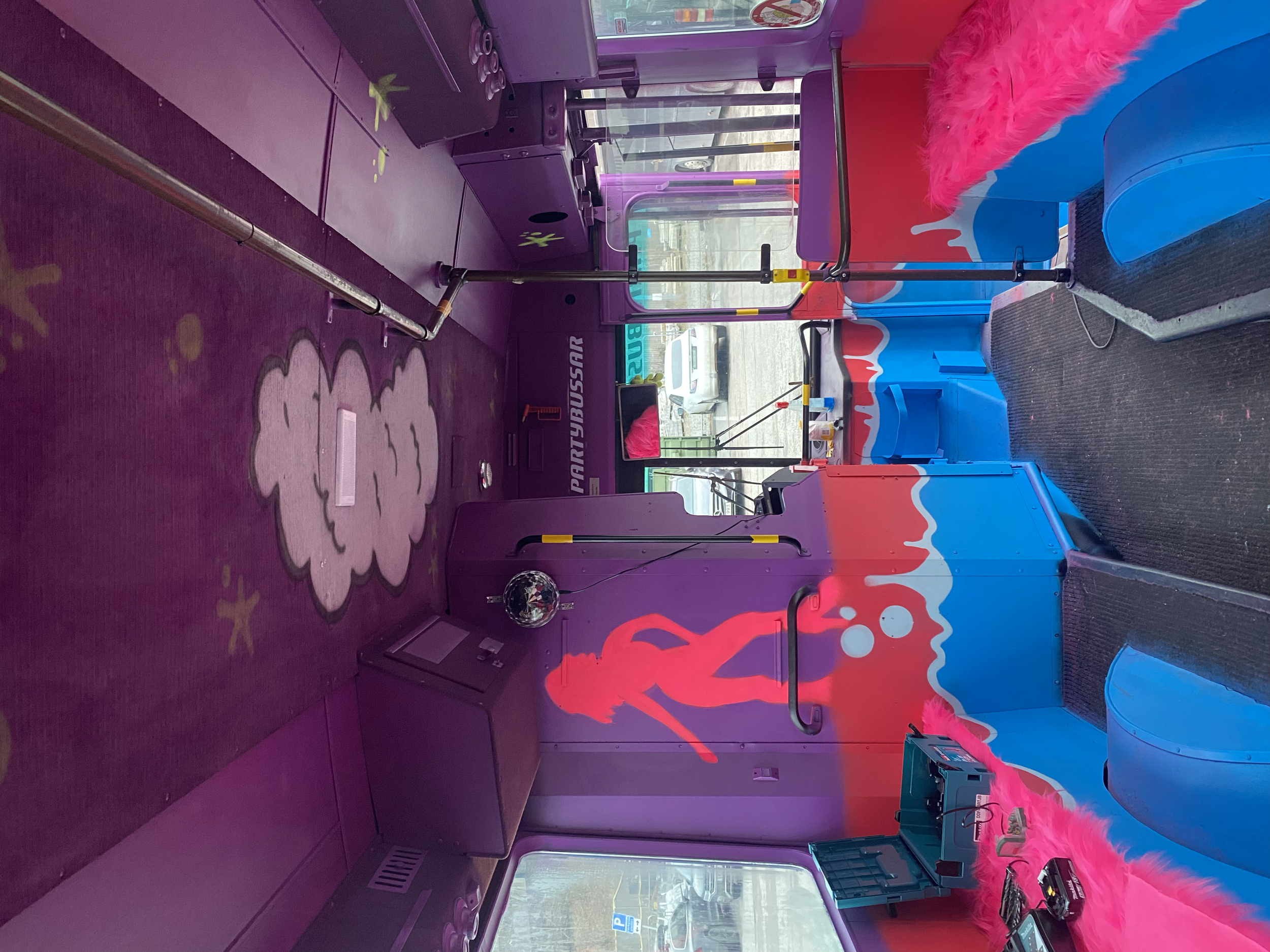 Interior of a colorful bus decorated with vibrant pink and blue designs, including a girl blowing bubbles, with pink faux fur trim around the edge, and a purple carpet and mural.
